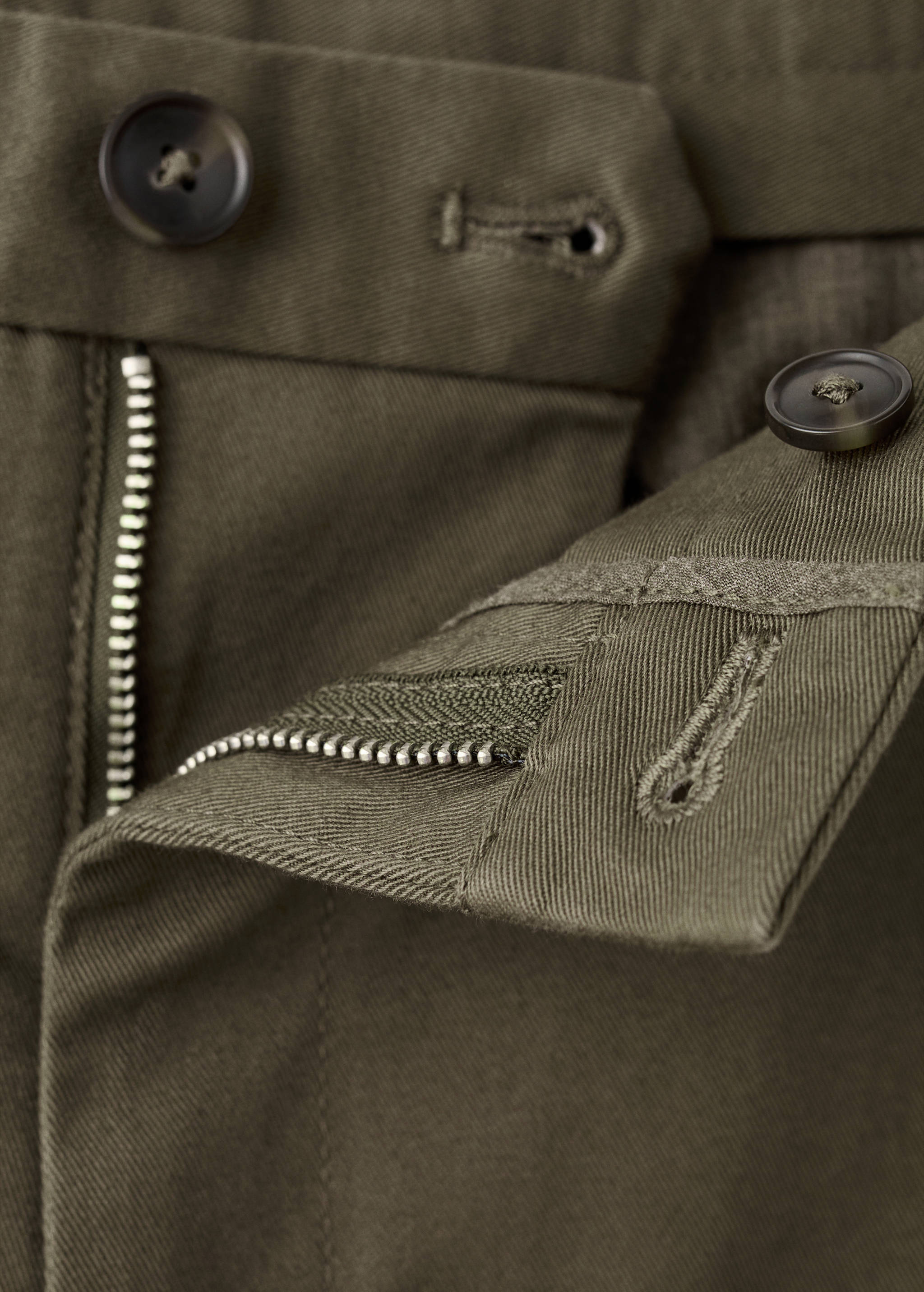 Close-up of olive green trousers waistband and zip fly.