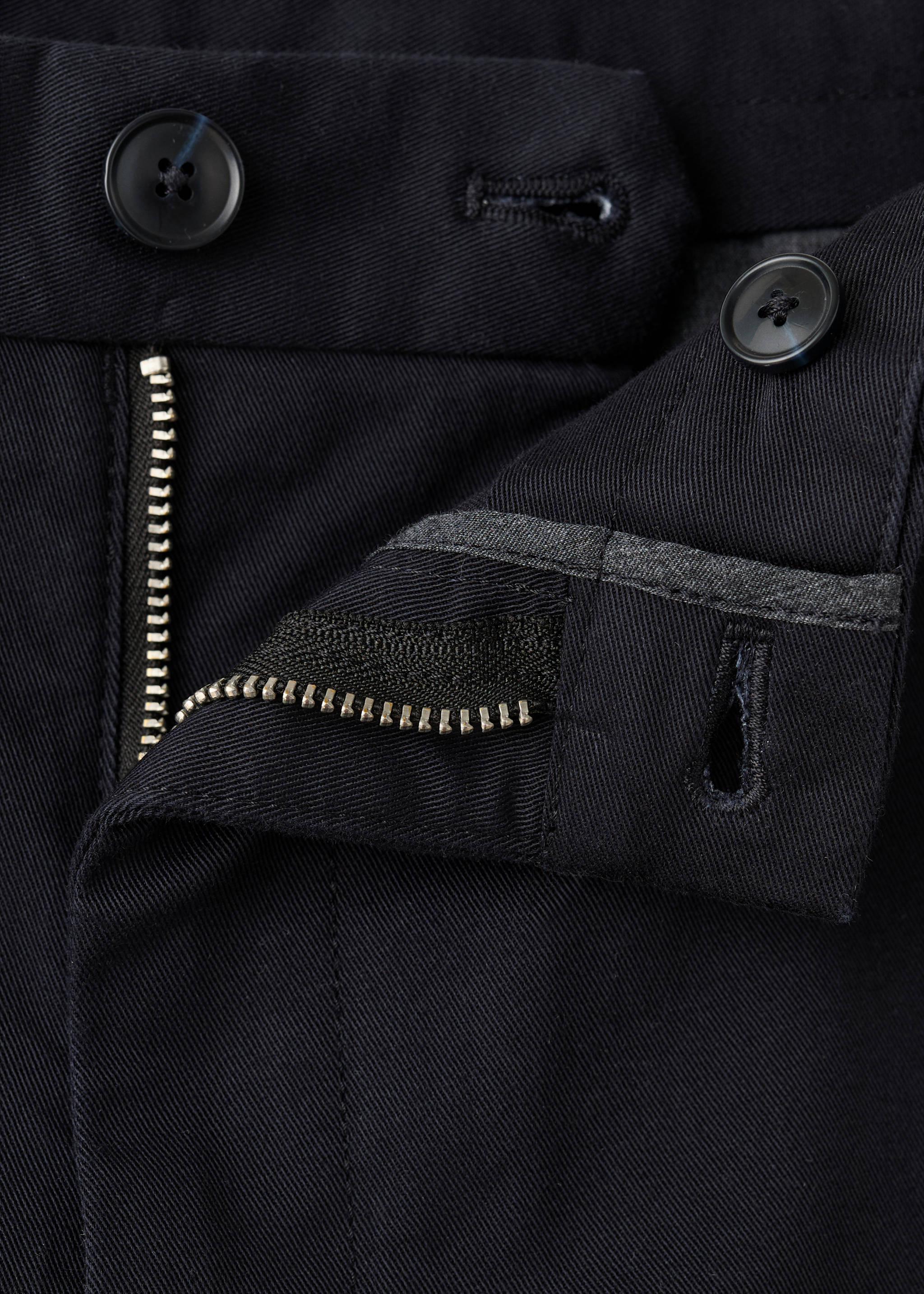 Close-up of dark blue trousers fabric, button fly, and waistband.