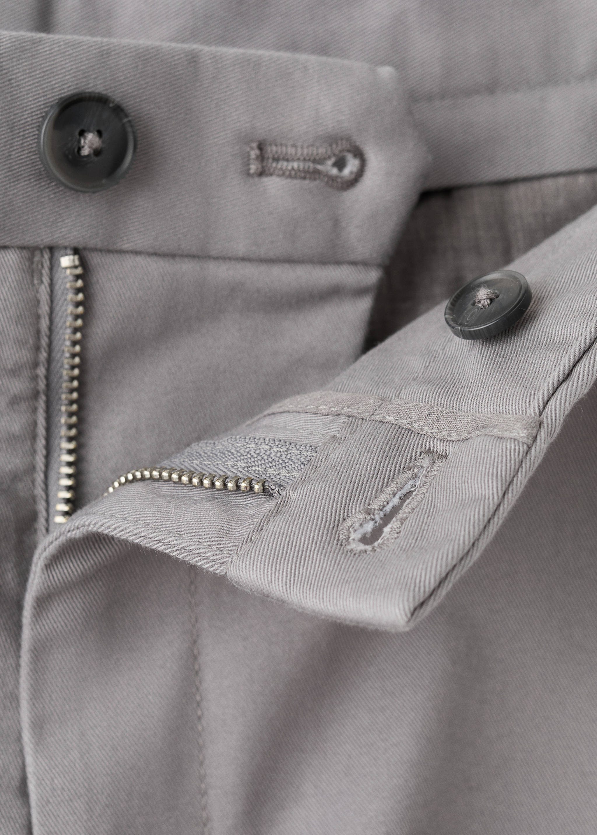 Close-up of grey trousers waistband and fastening details