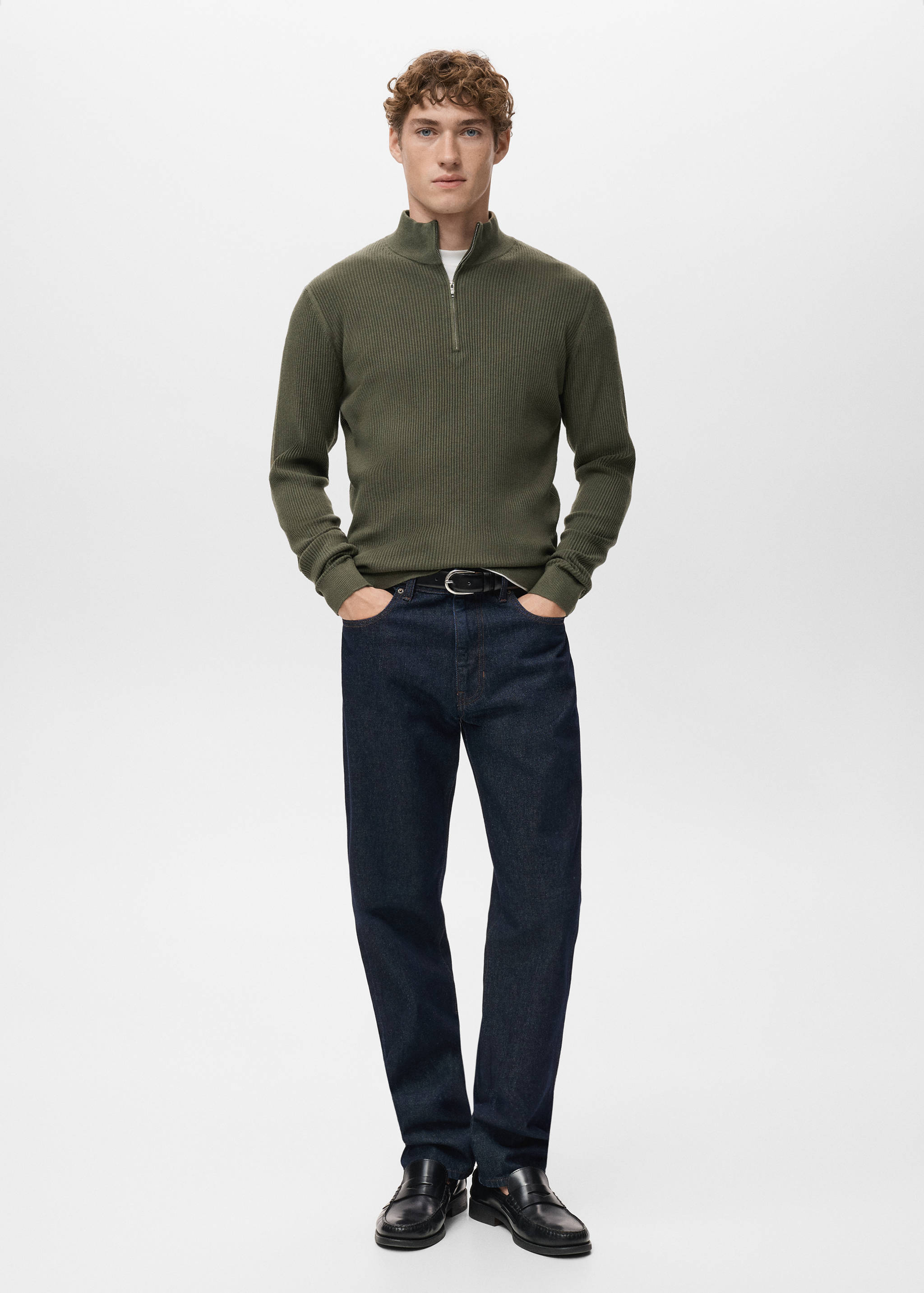 Khaki green ribbed zip-neck jumper worn with dark blue denim trousers.