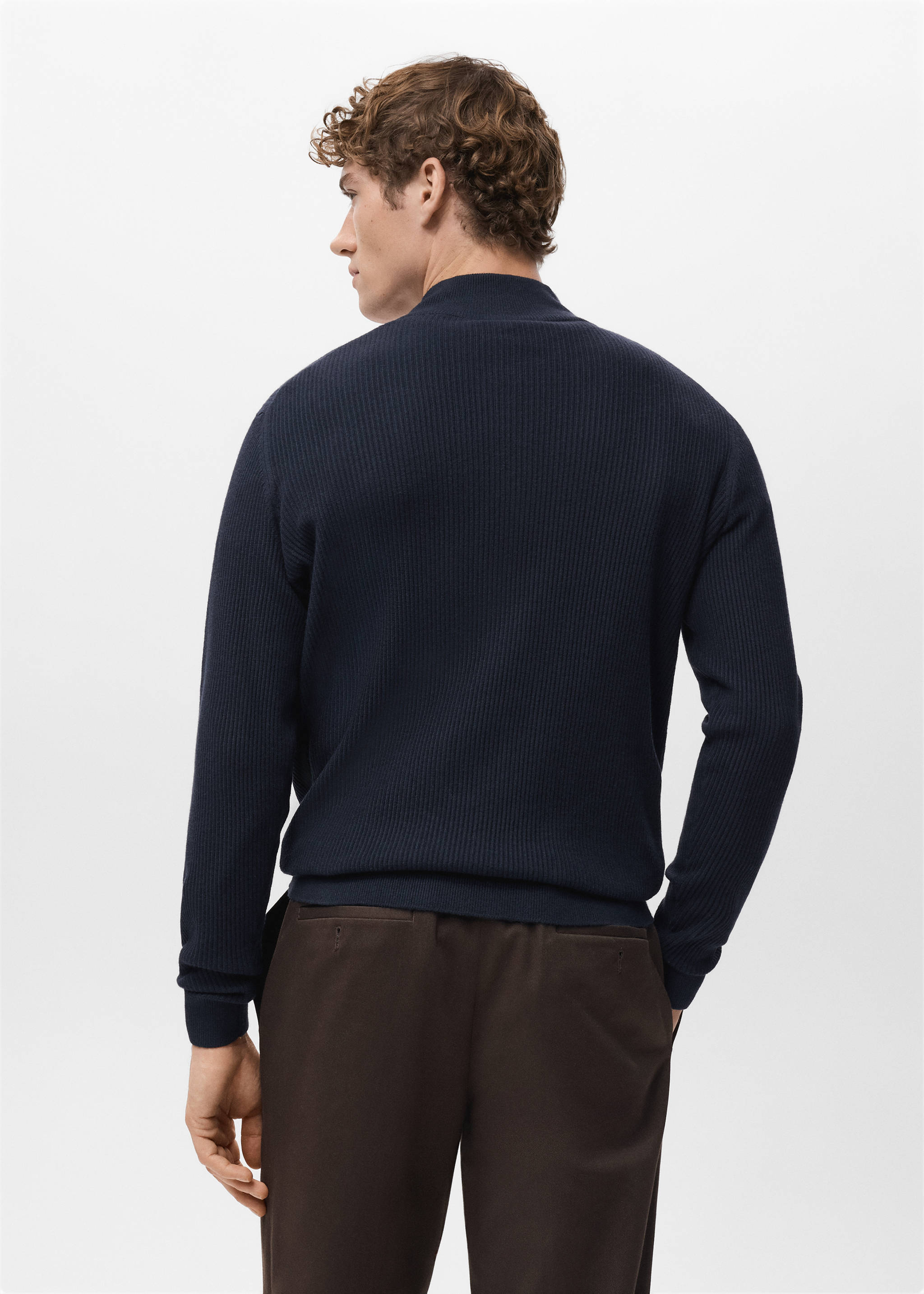 Navy blue ribbed knitted jersey seen from the back, paired with trousers.