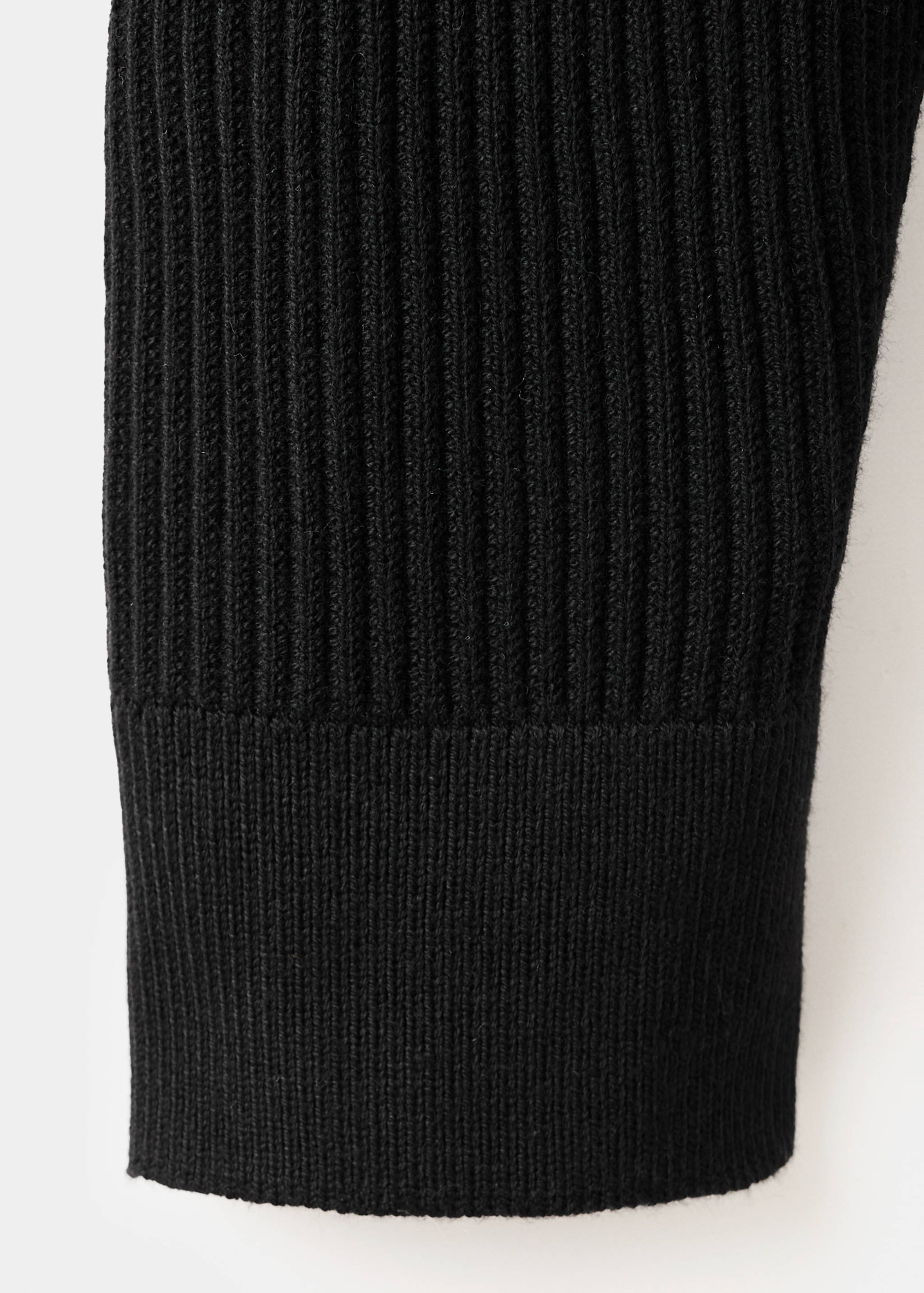 Close-up of black knitted jumper showing ribbed texture and cuff.