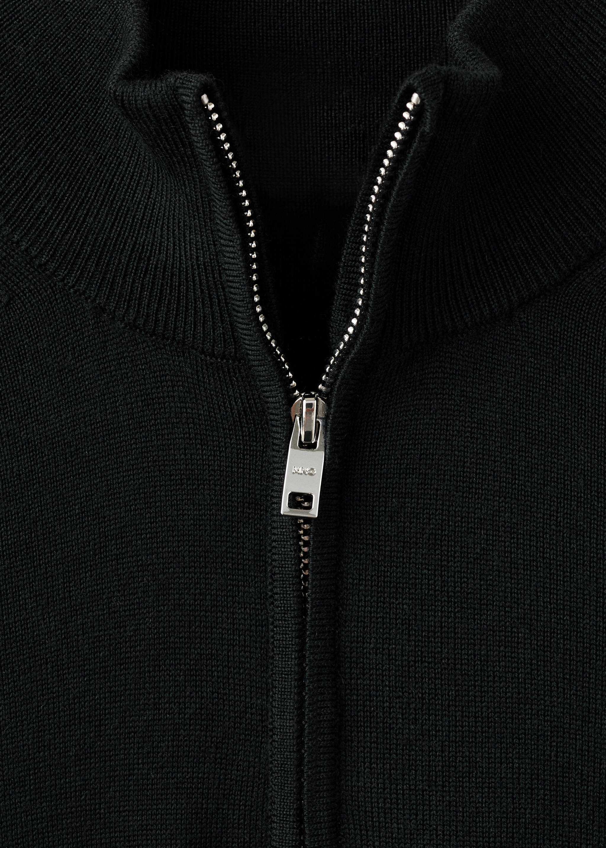 Close-up of a black jersey with a high ribbed collar and silver half-zip.