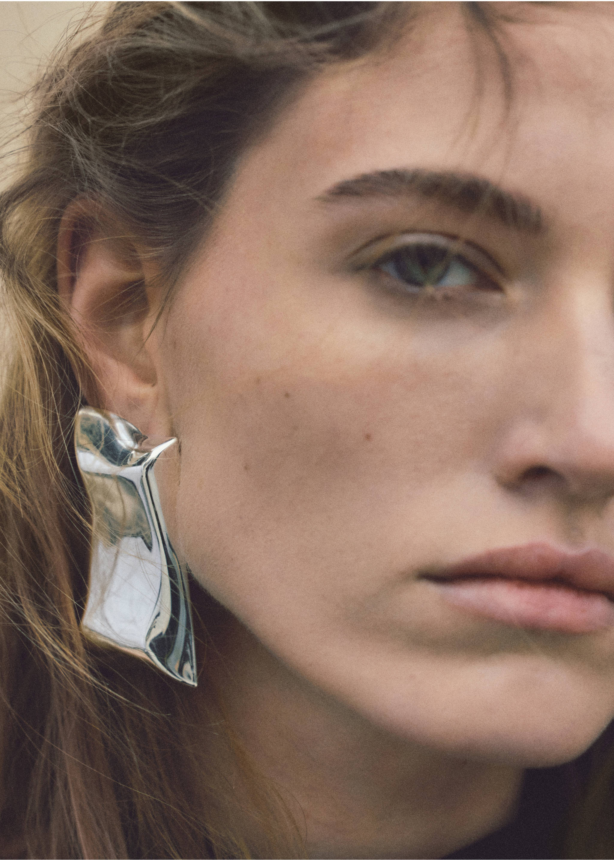 Close-up of a model wearing an oversized, sculptural silver earring., Silver. Ref: 27042930-00.