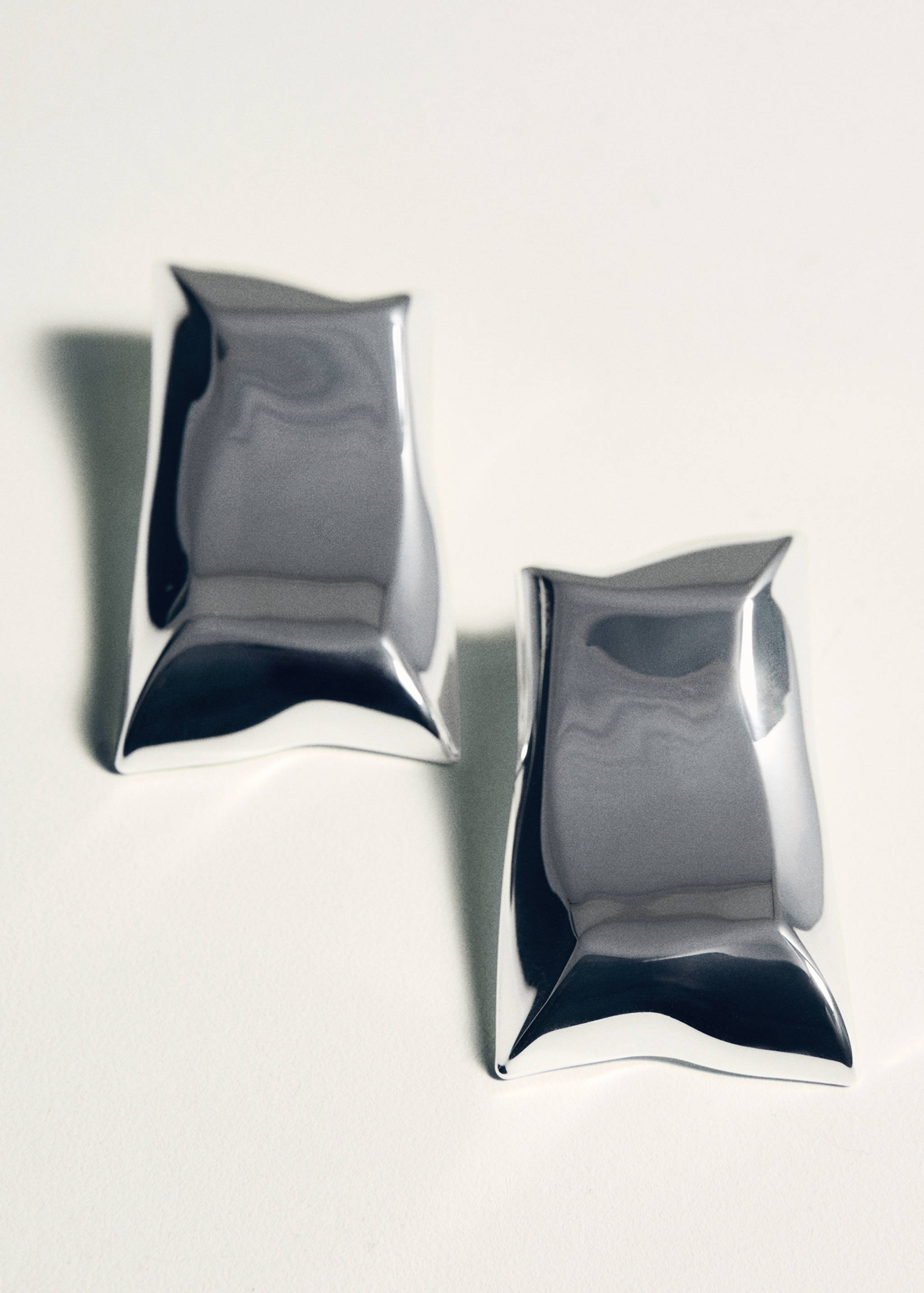 Shiny silver-coloured metal earrings with a curved geometric shape.