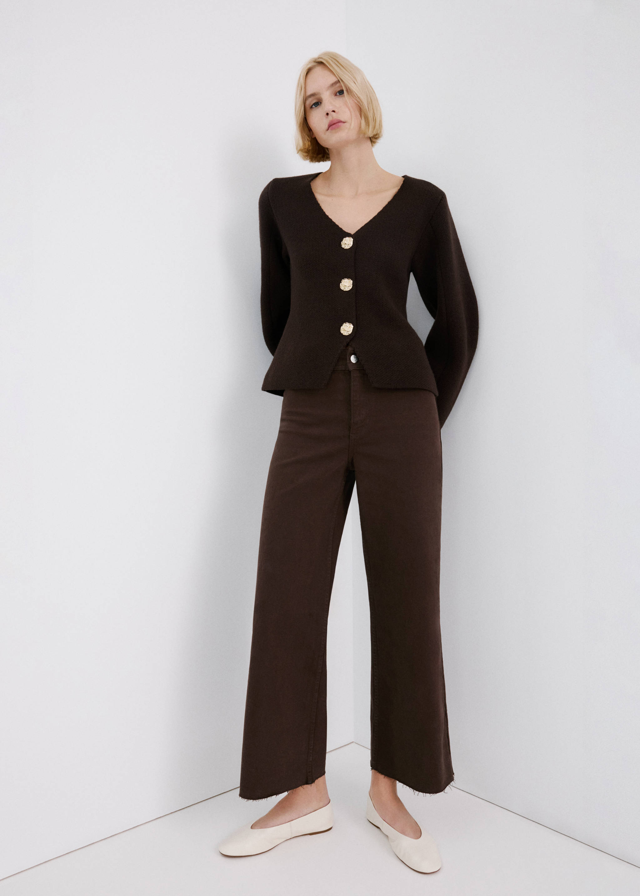 Brown straight-leg trousers with cropped raw hems, worn with a dark brown cardigan.