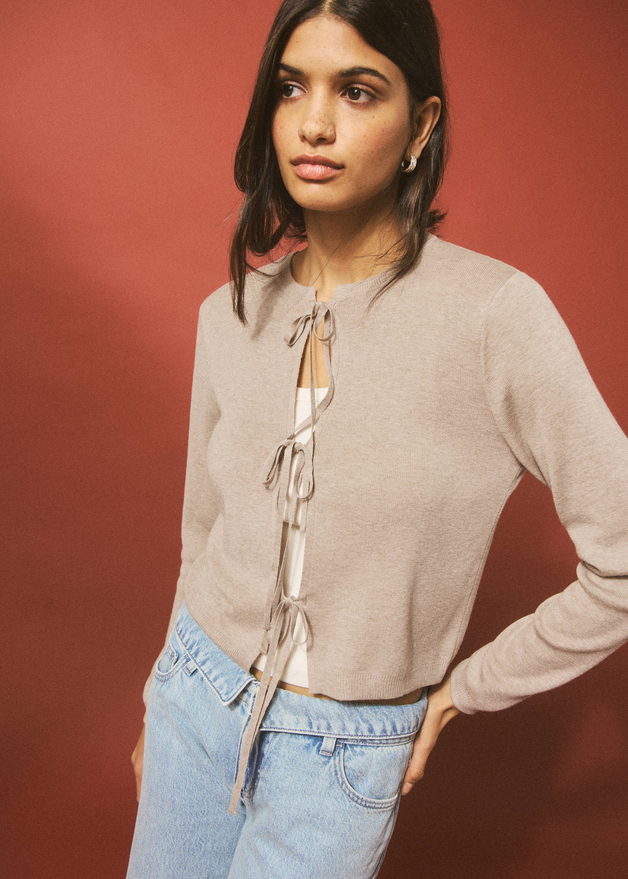 Beige knit cardigan with front ties, layered over a white top and blue jeans.