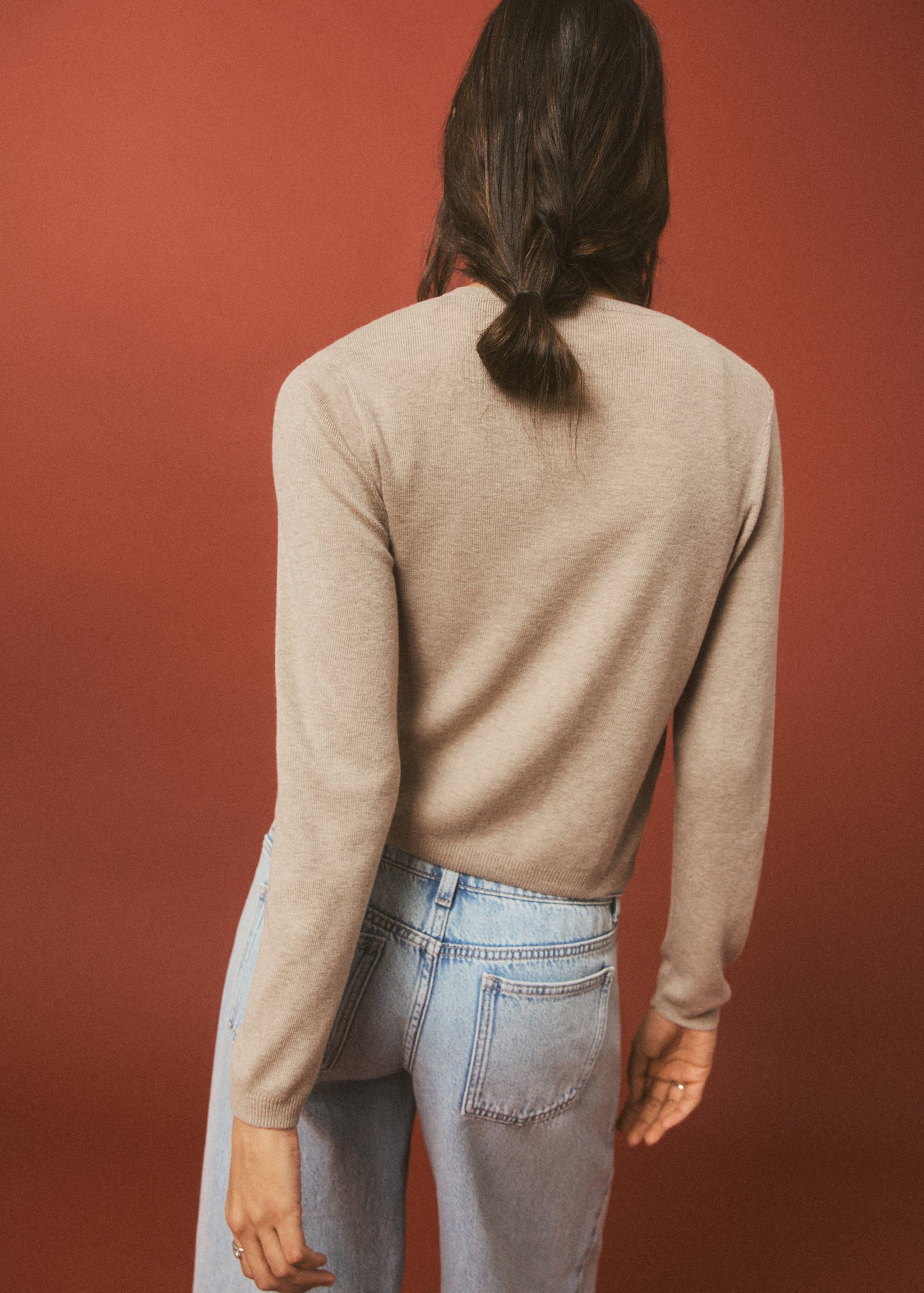 Beige knitted cardigan shown from the back, worn with light blue jeans.