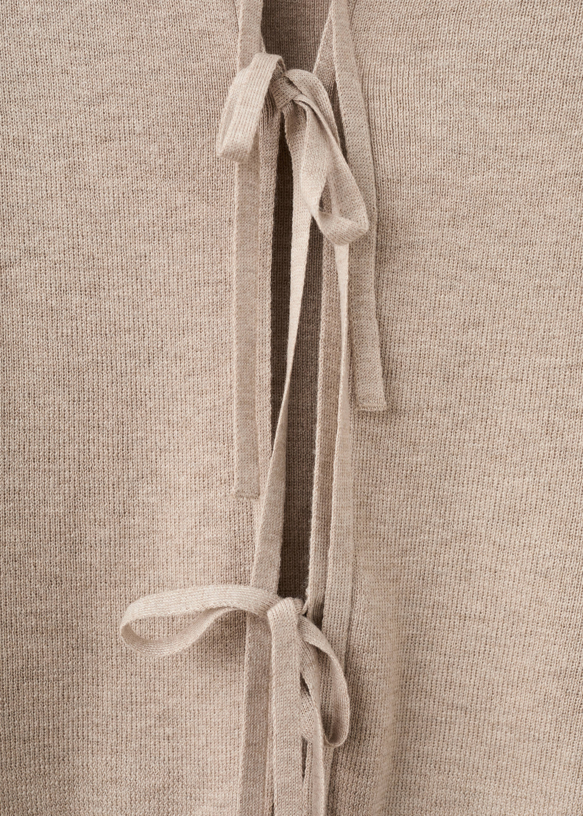 Close-up of a beige knit cardigan featuring thin front tie closures.