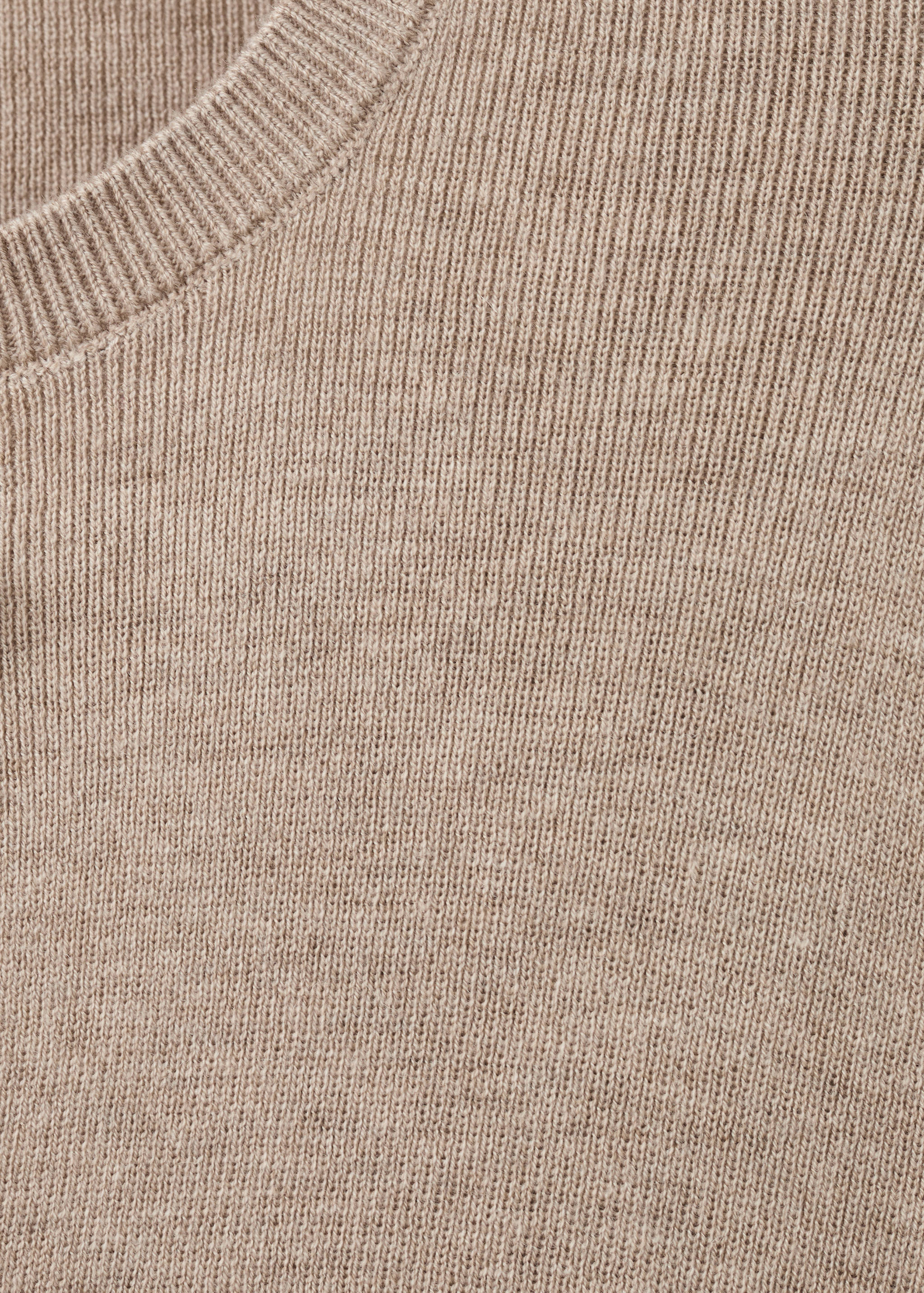Close-up of the fine-knit fabric and ribbed neckline of a beige cardigan.