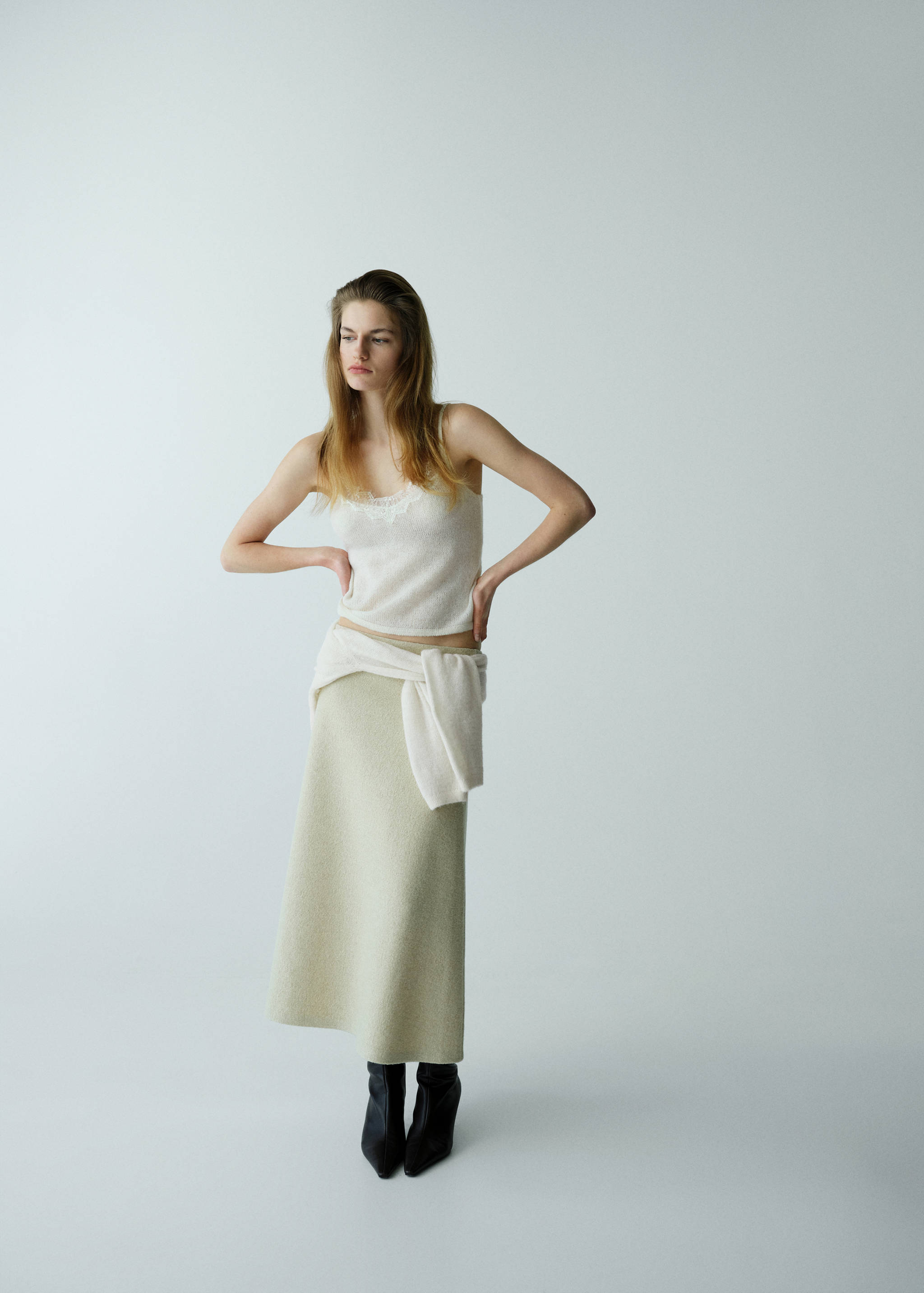 Cream lace-trim camisole top worn with a pale green midi skirt and tied knit sweater.