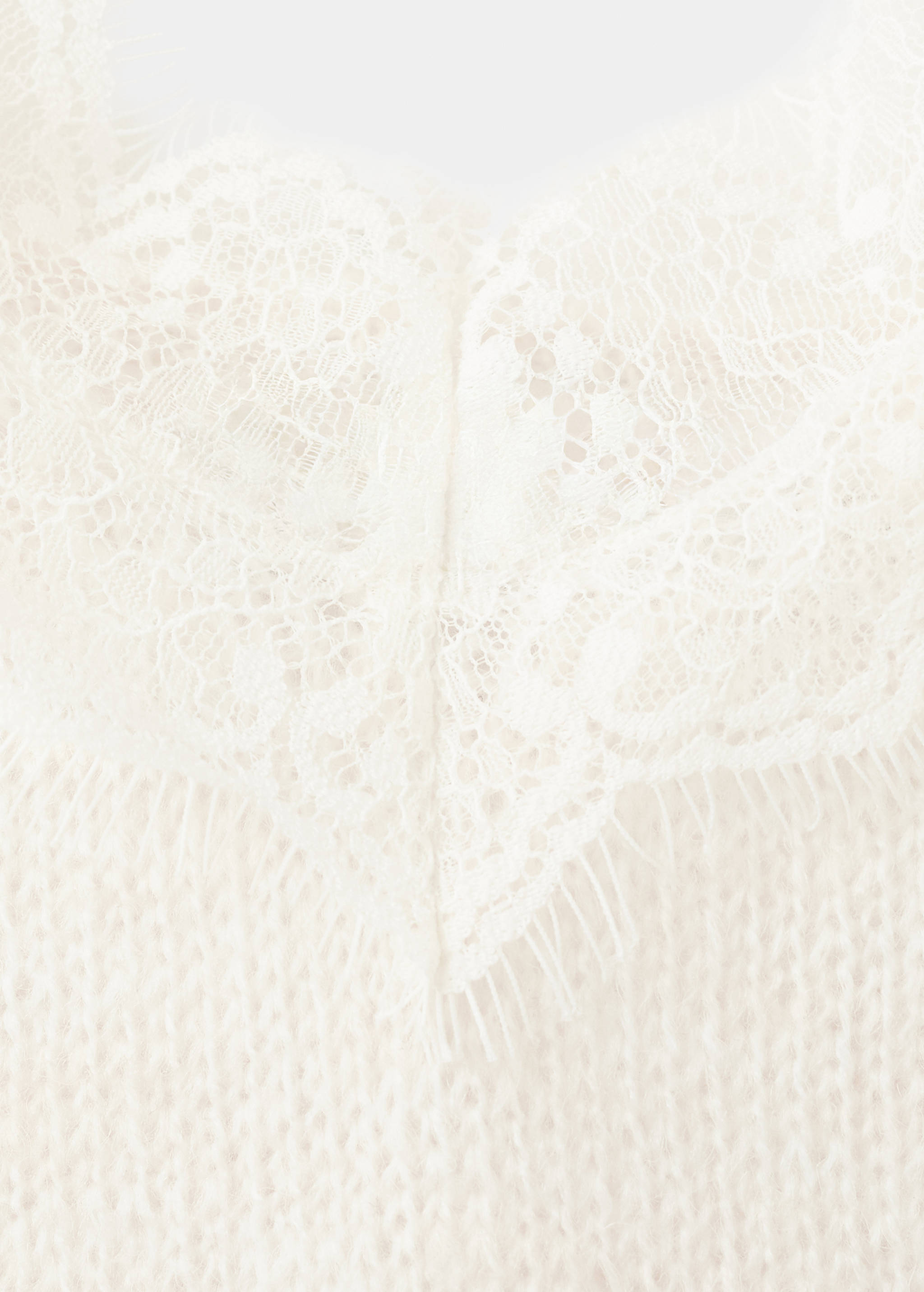 Close-up of cream knit top featuring a V-neckline with lace trim.