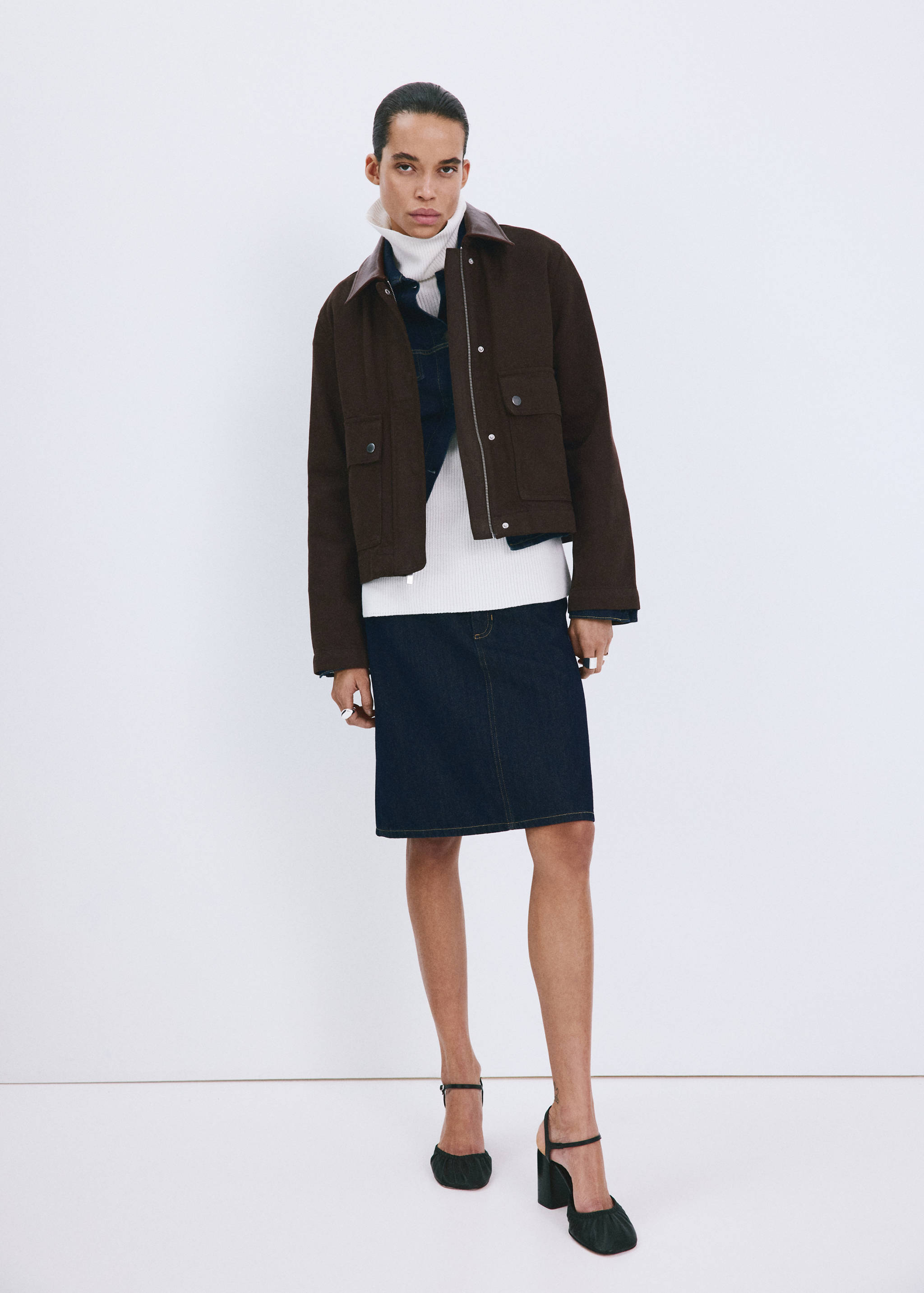 Brown cropped jacket with leather collar worn with a denim jacket, turtleneck, skirt, and heels.