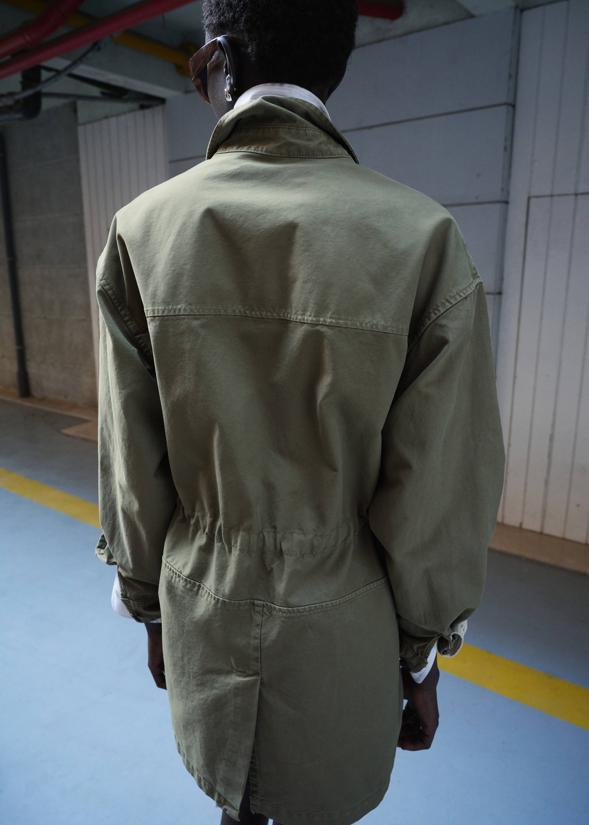 Parka verde oliva de espaldas con cordón ajustable en la cintura y cuello alto.