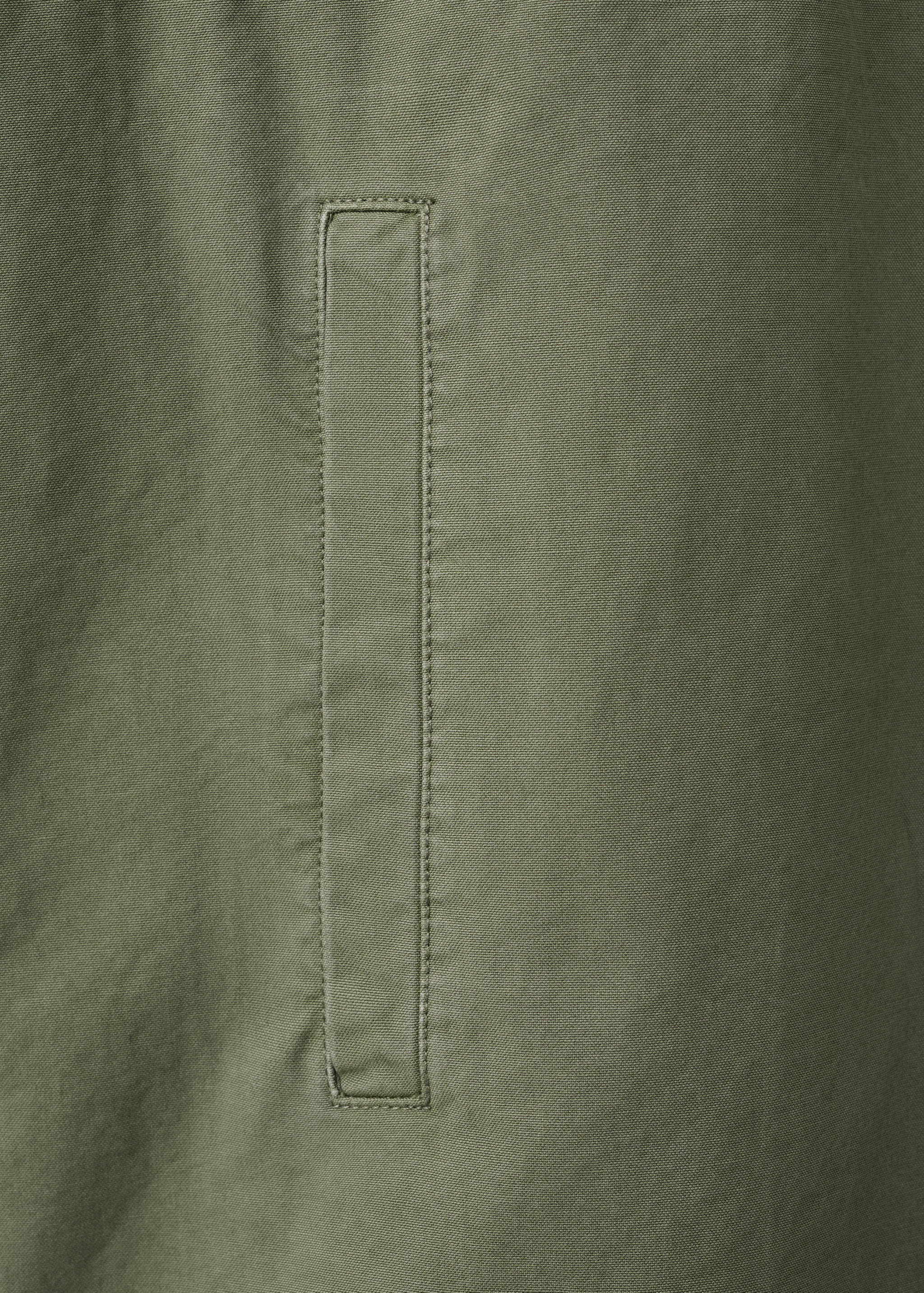 Primer plano del tejido de la parka verde que destaca la textura y el bolsillo de vivo.