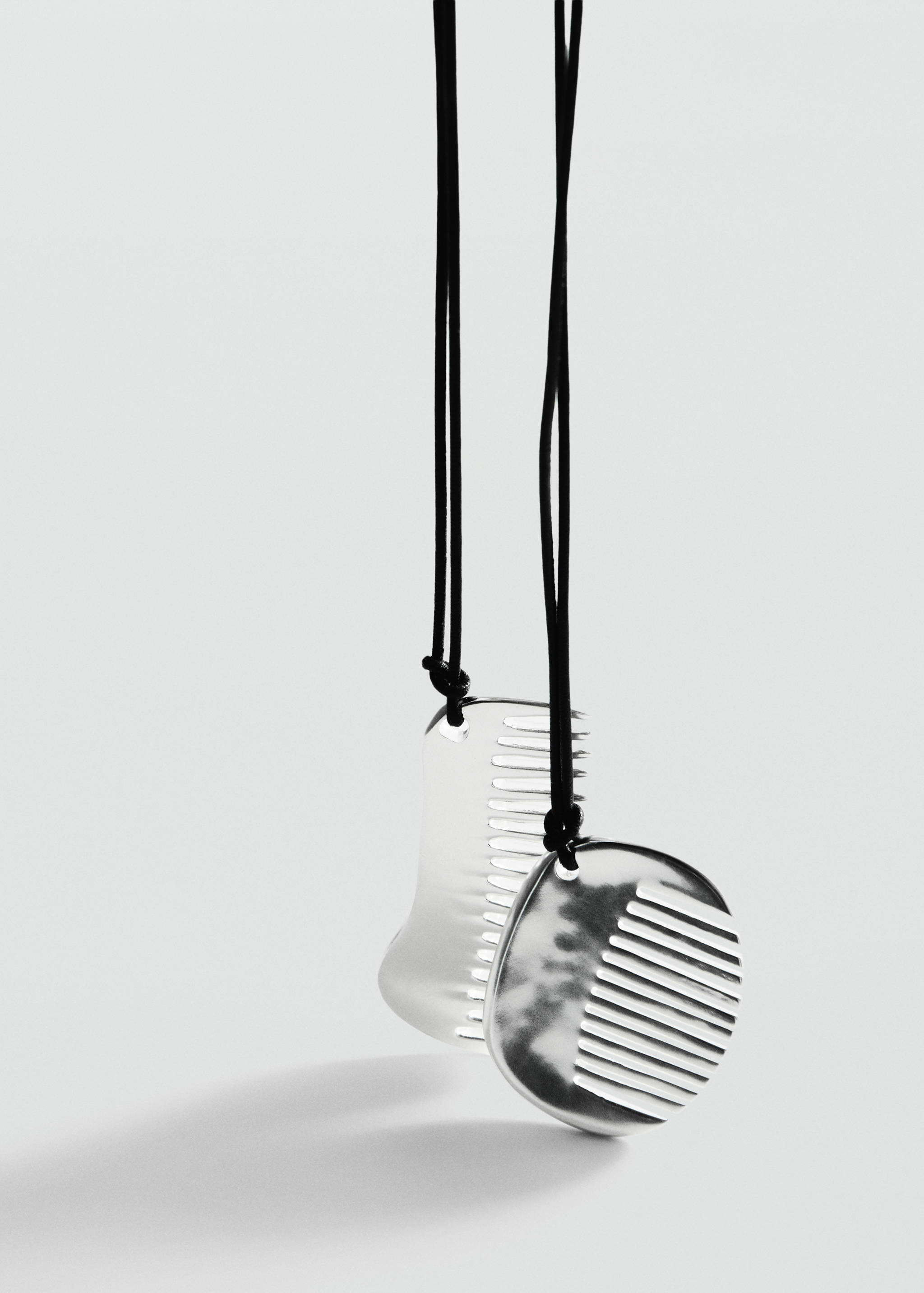 Silver-coloured comb pendant necklace on a black cord.