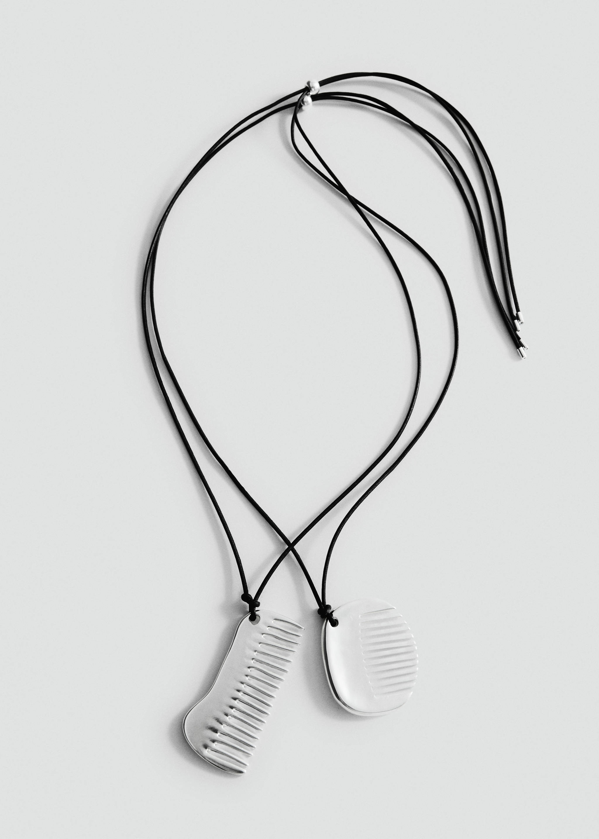 Silver-coloured metal comb pendant necklace on black cords.