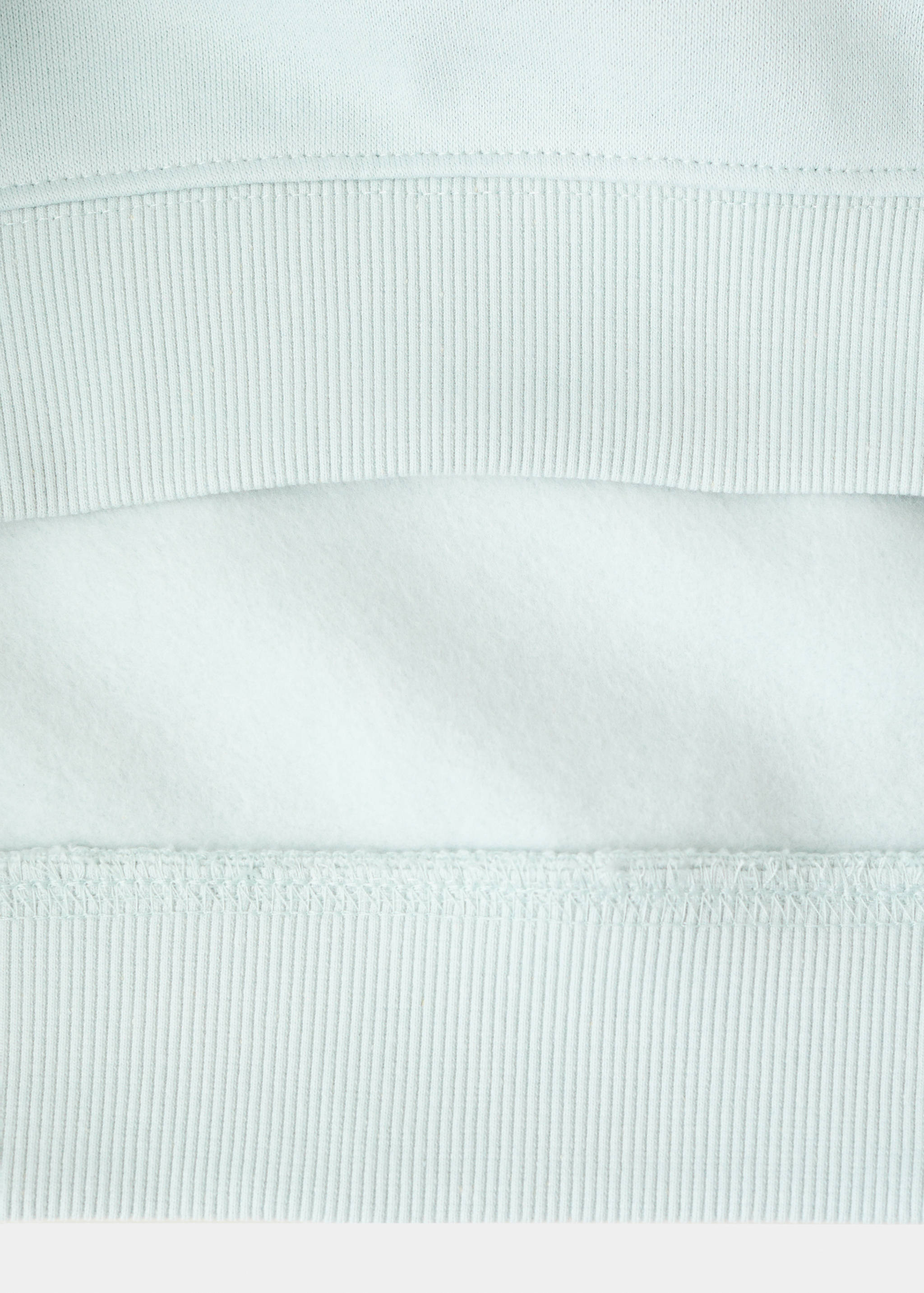 Close-up of the fabric texture and ribbed hem of a light blue sweatshirt.