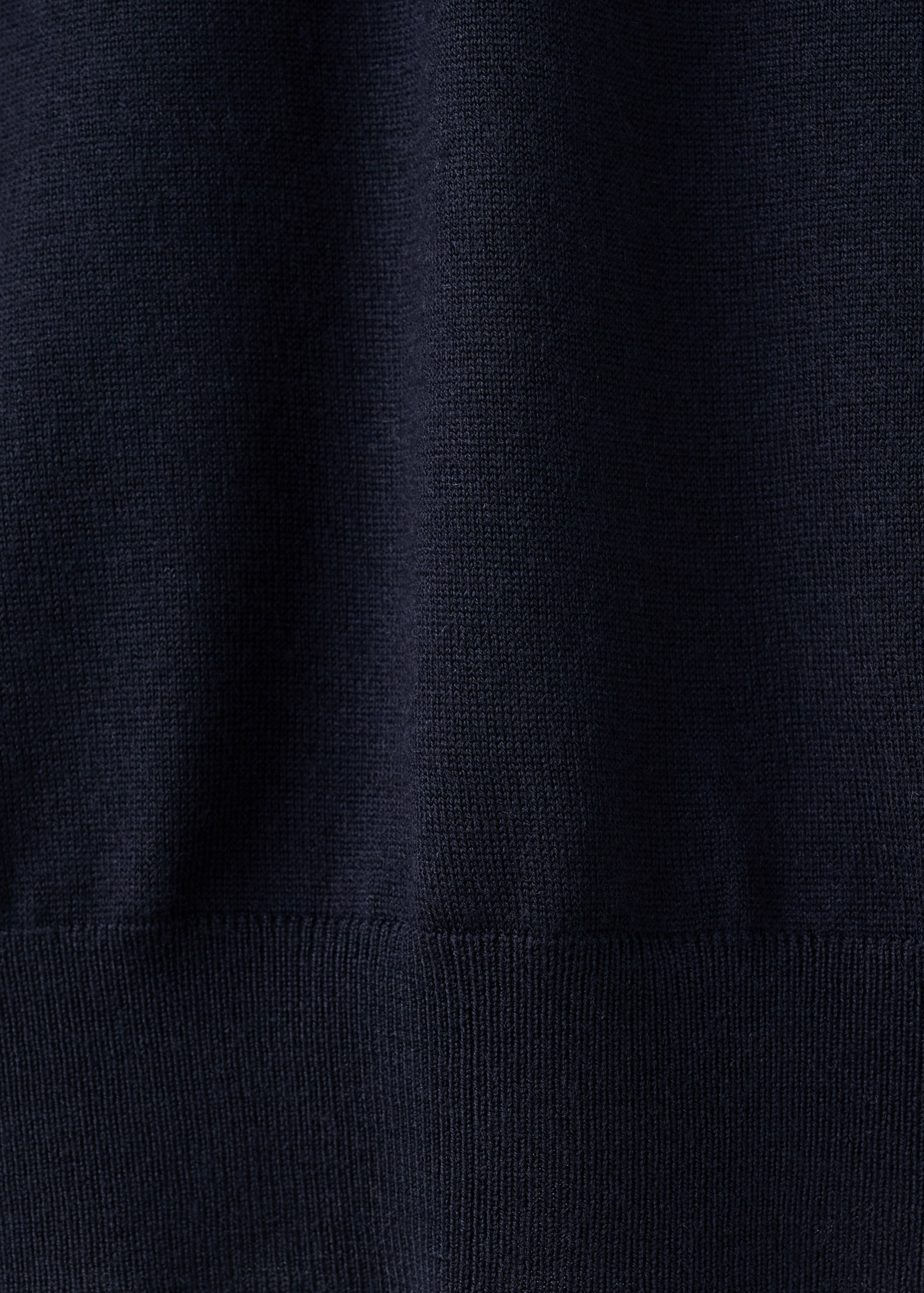 Close-up of the fine knit texture and ribbed hem of a dark navy blue polo.
