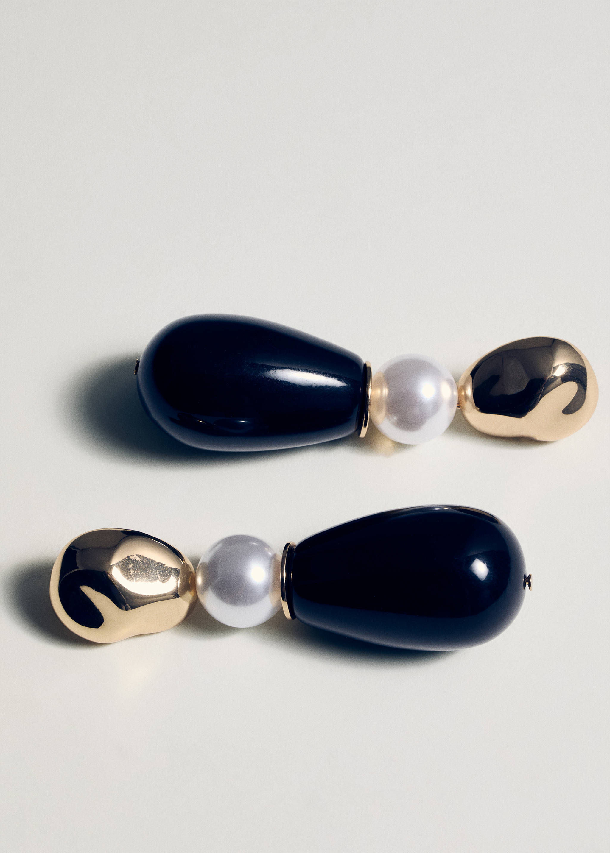 Drop earrings featuring a gold-tone organic stud, a white bead, and a black teardrop pendant.