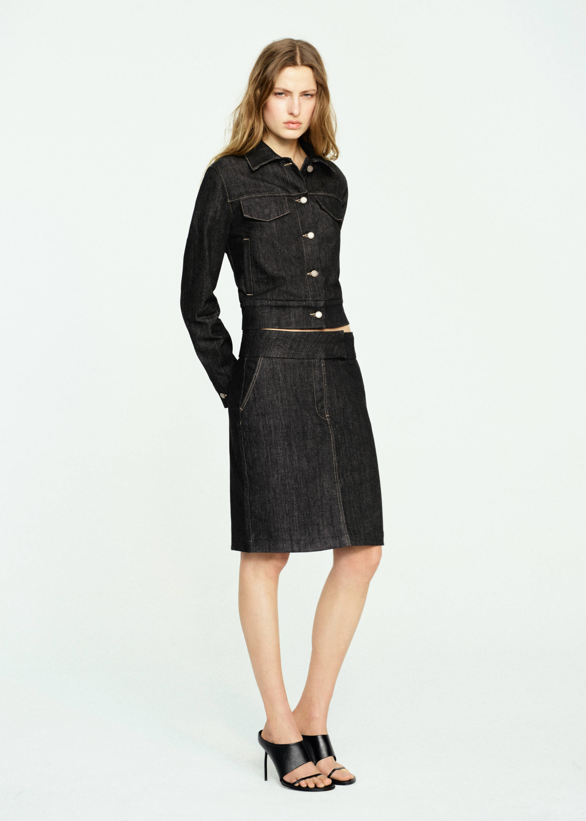 Falda midi recta de tejido vaquero oscuro, combinada con una chaqueta a juego.
