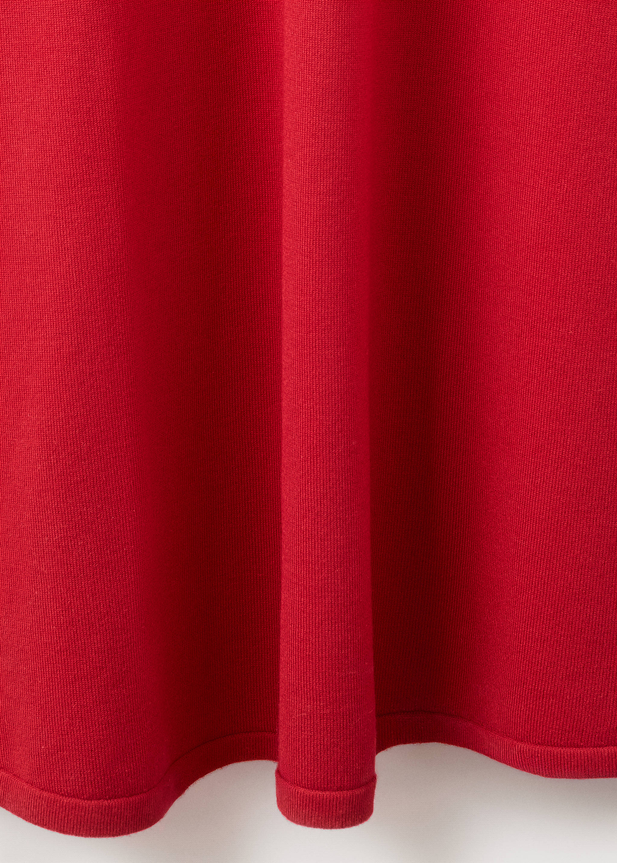 Close-up of the red knit fabric and ribbed hem of a dress.