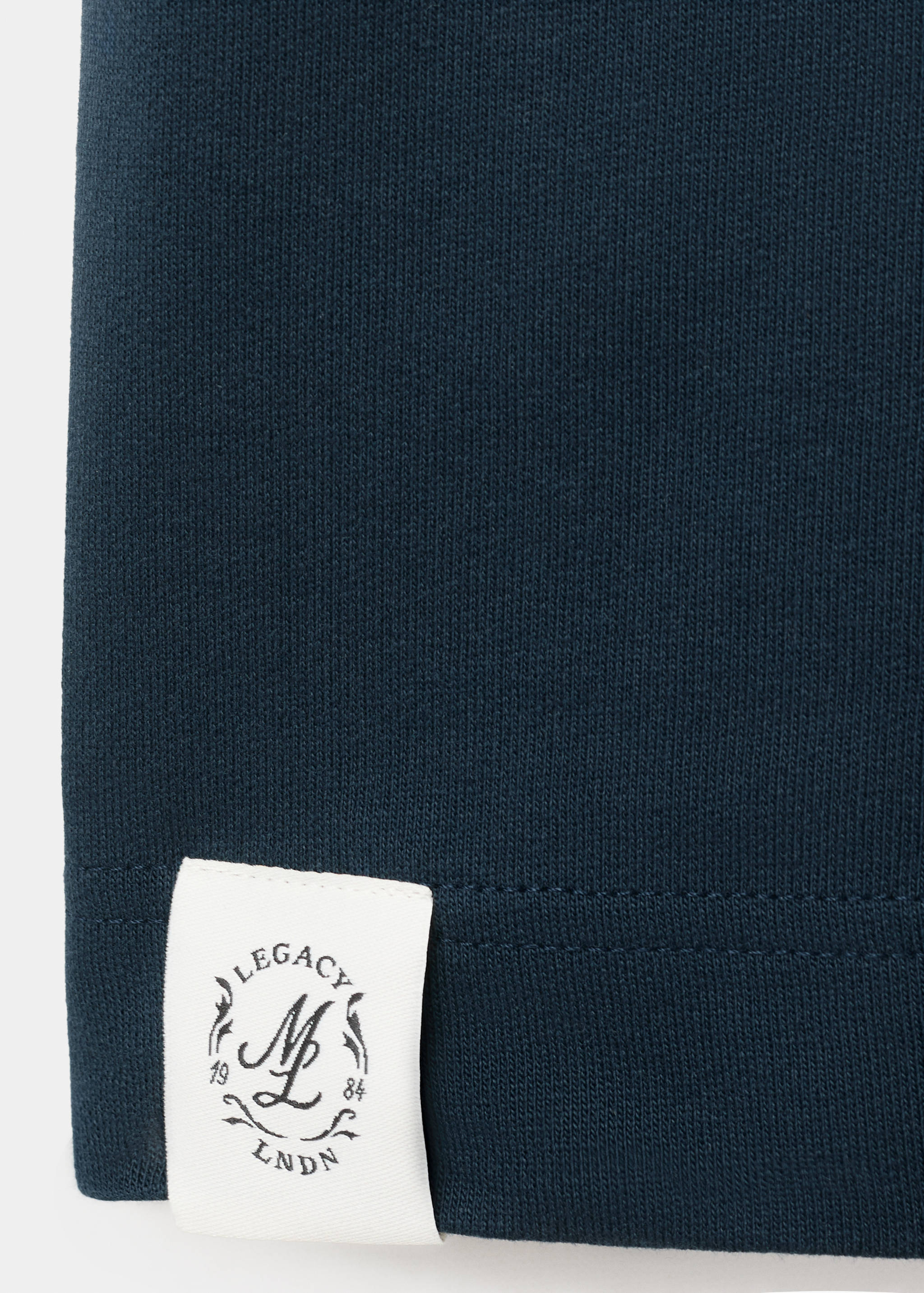 Close-up of navy blue t-shirt fabric with a branded white patch detail on the hem.