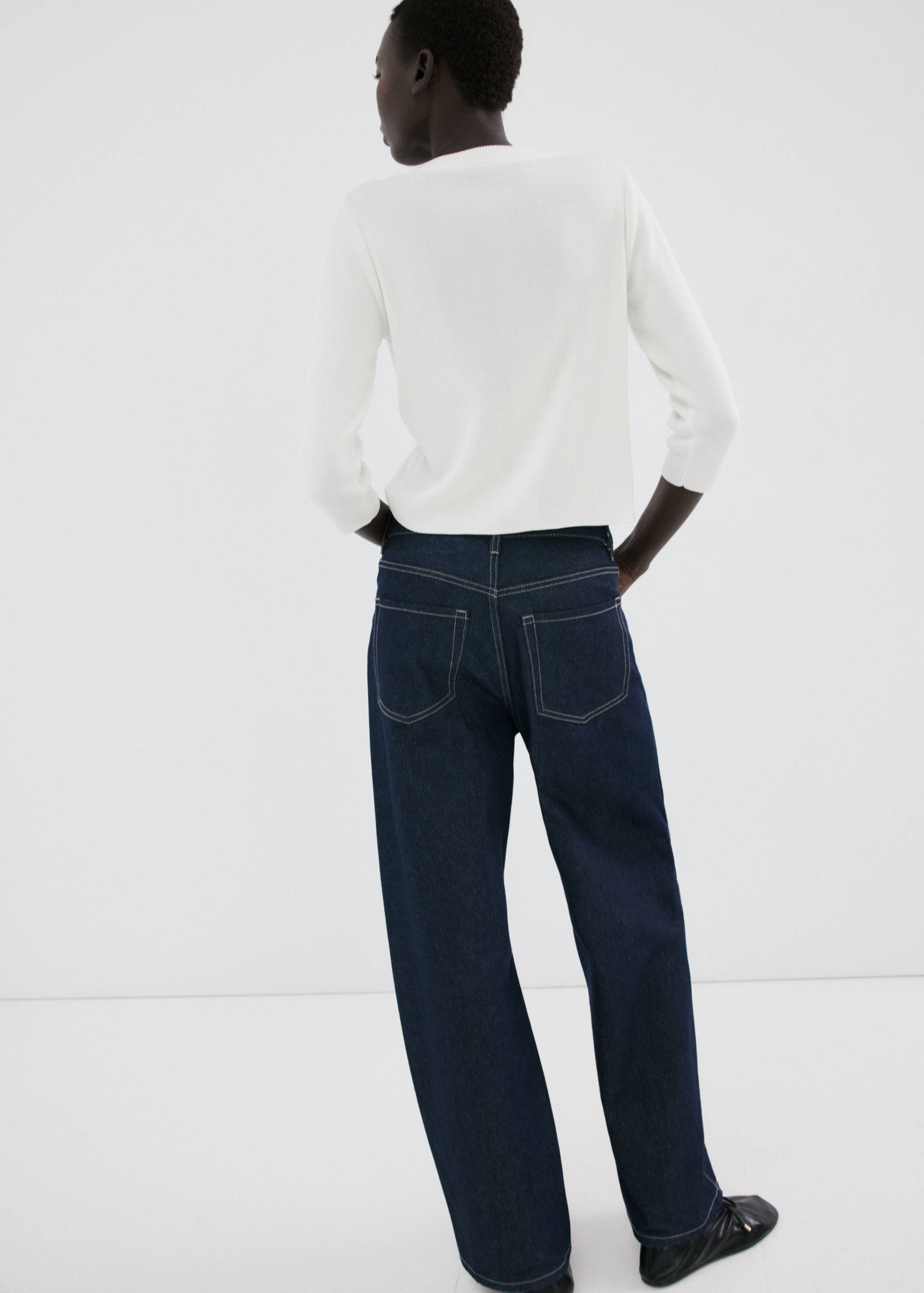 Back view of a white cardigan worn with dark blue denim trousers.