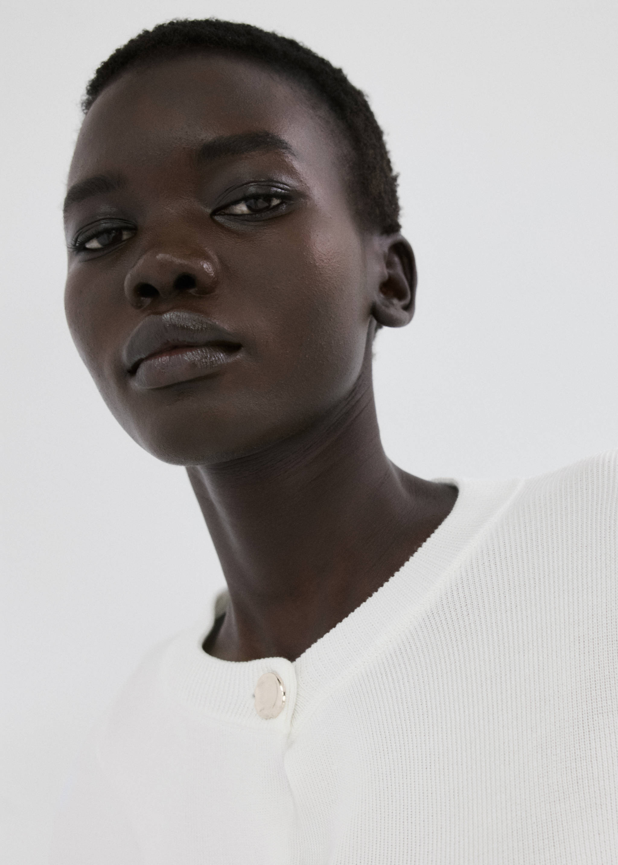 Close-up of a white knitted cardigan with a metallic button.