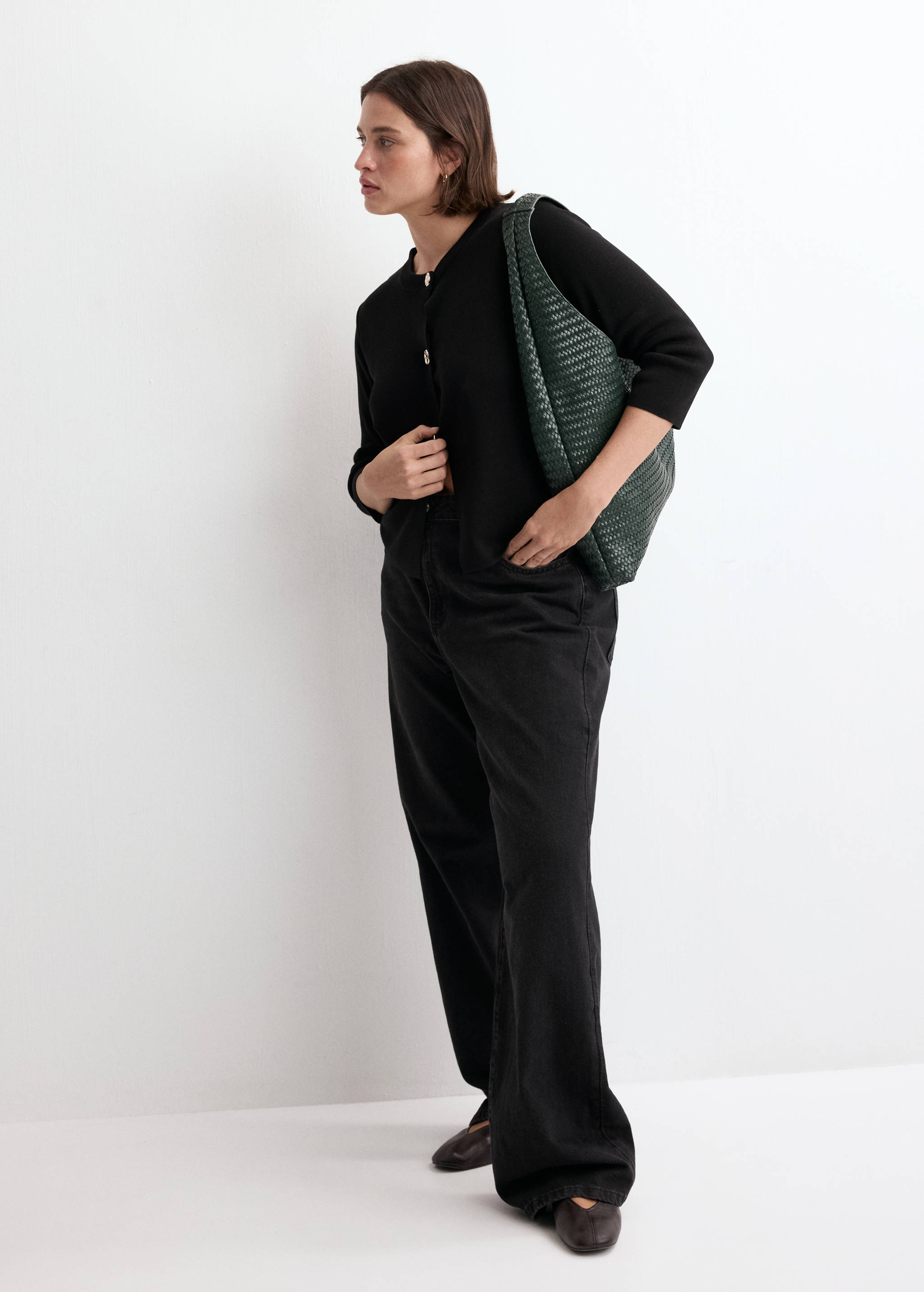 Black knit cardigan with gold buttons, worn with dark trousers and a green woven bag