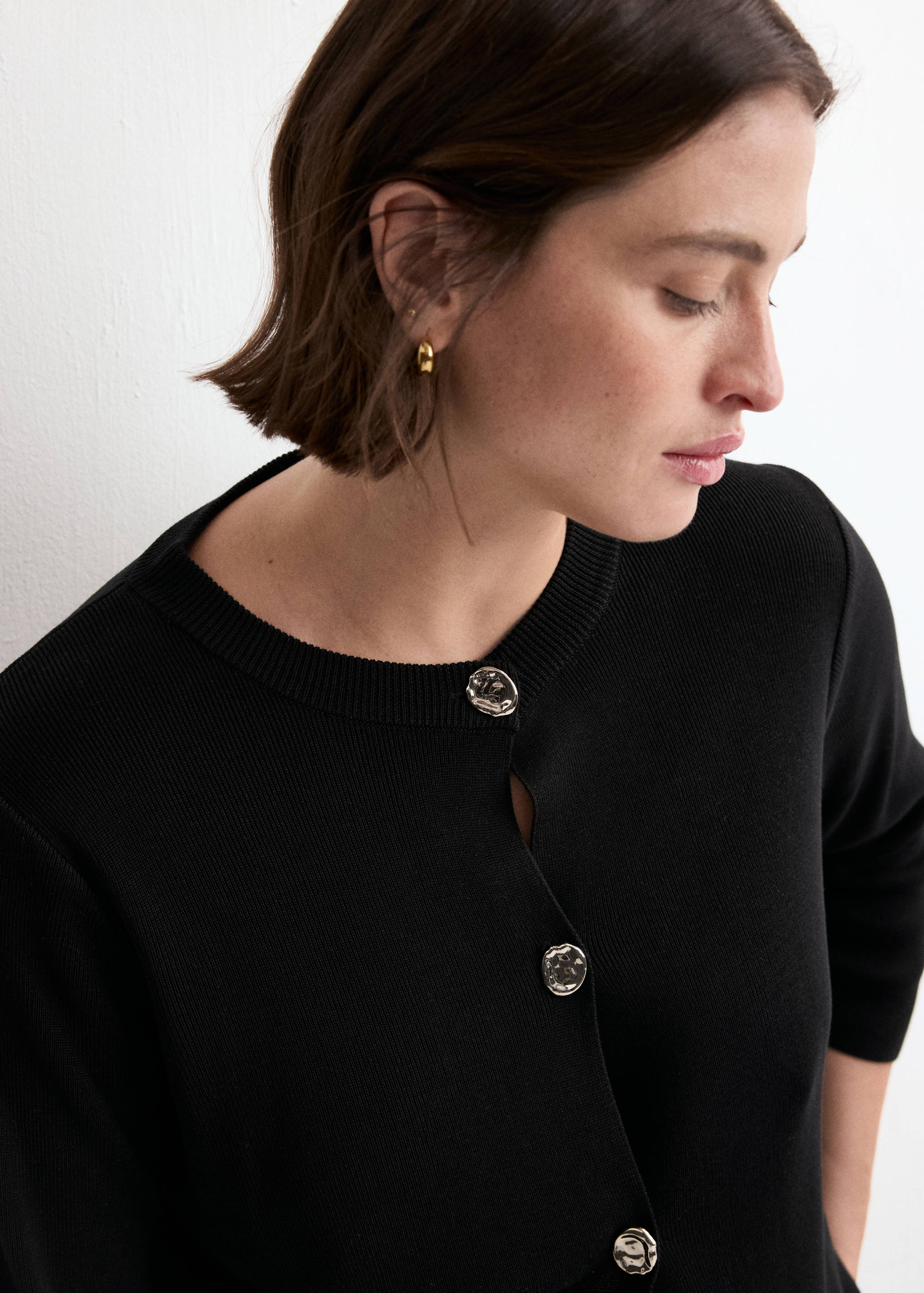 Black cardigan with a round neck and ornate silver buttons.