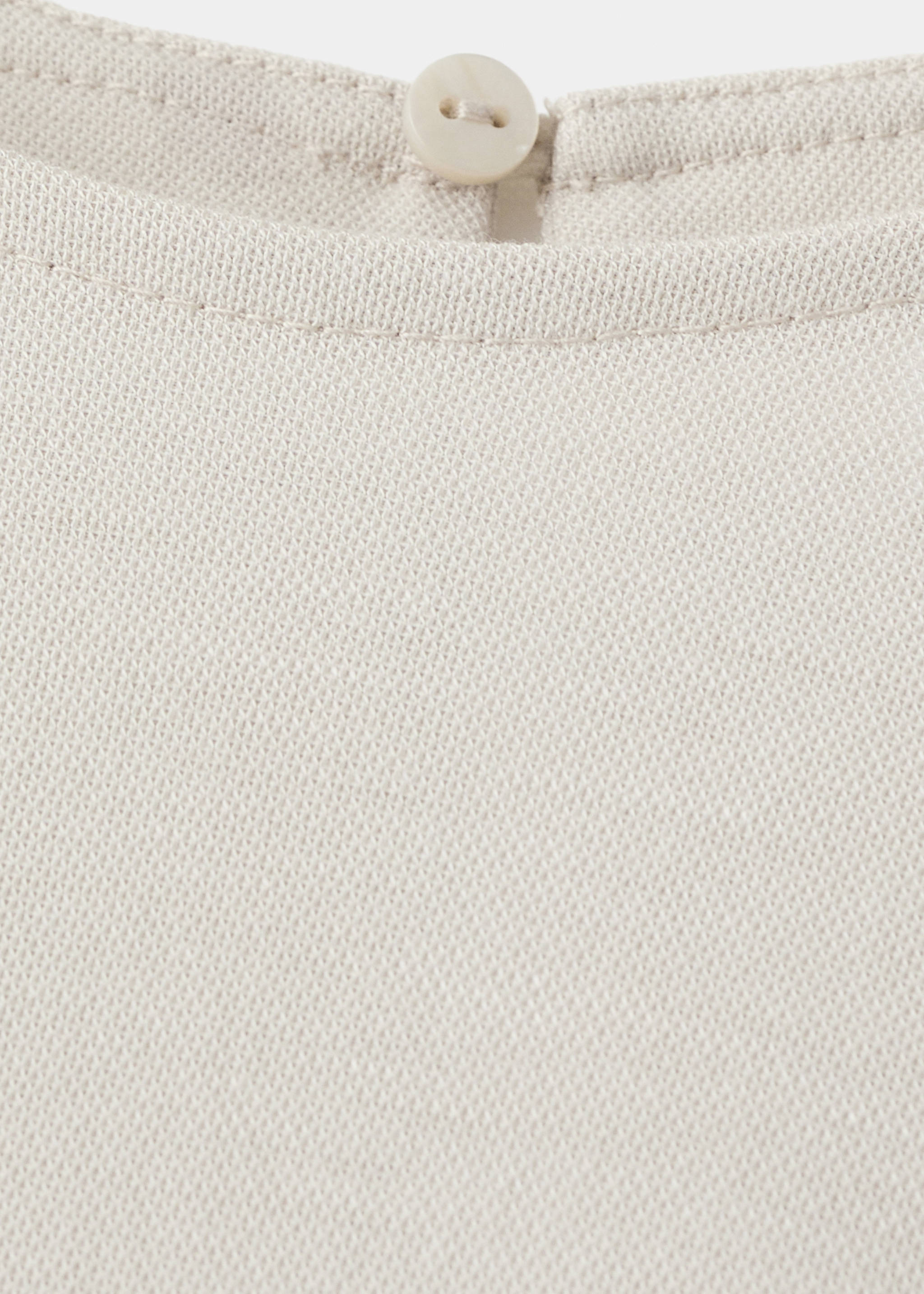 Close-up of a beige dress neckline with a button detail.