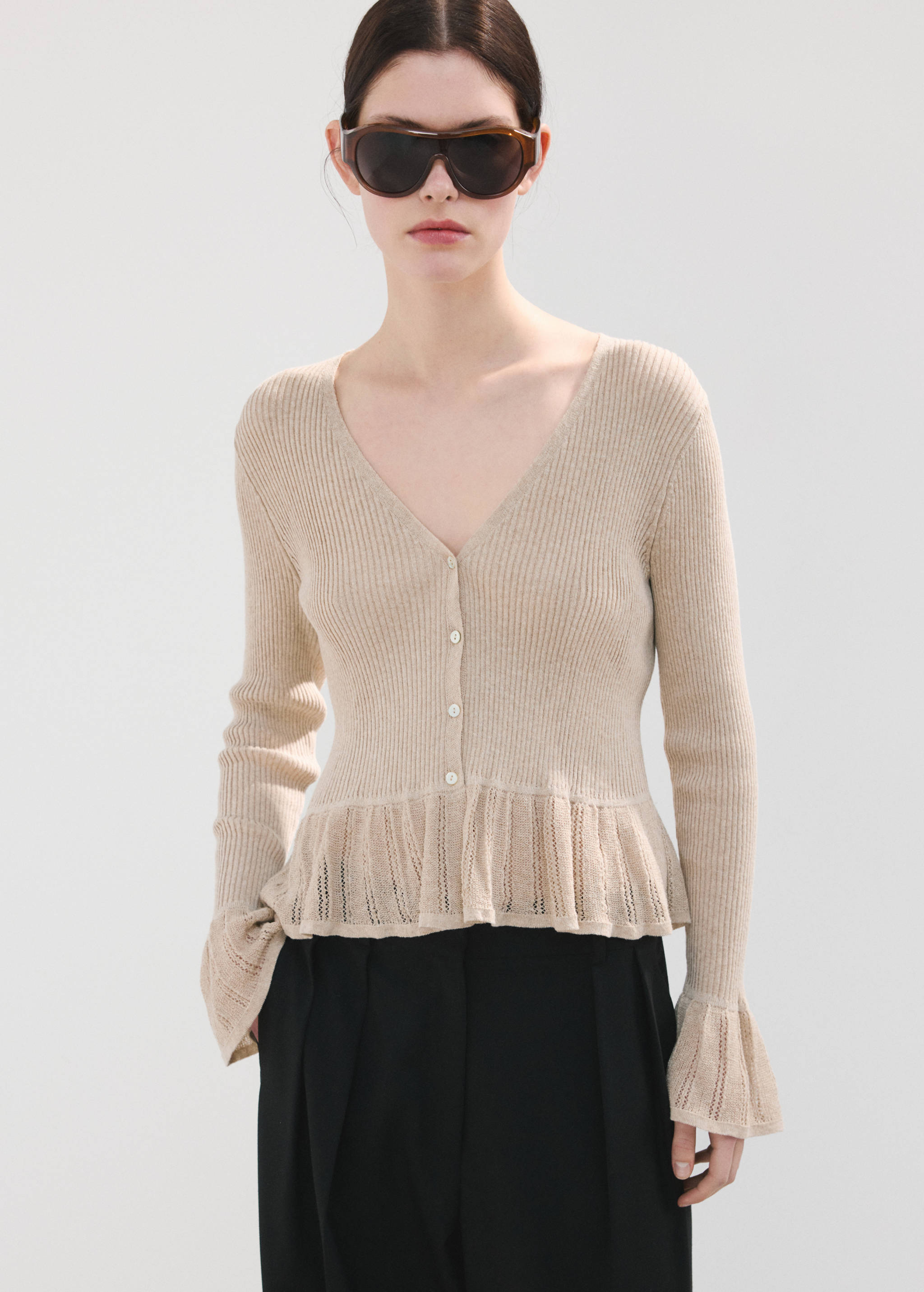 Beige ribbed knit cardigan with V-neck, button fastening, and ruffled hem.