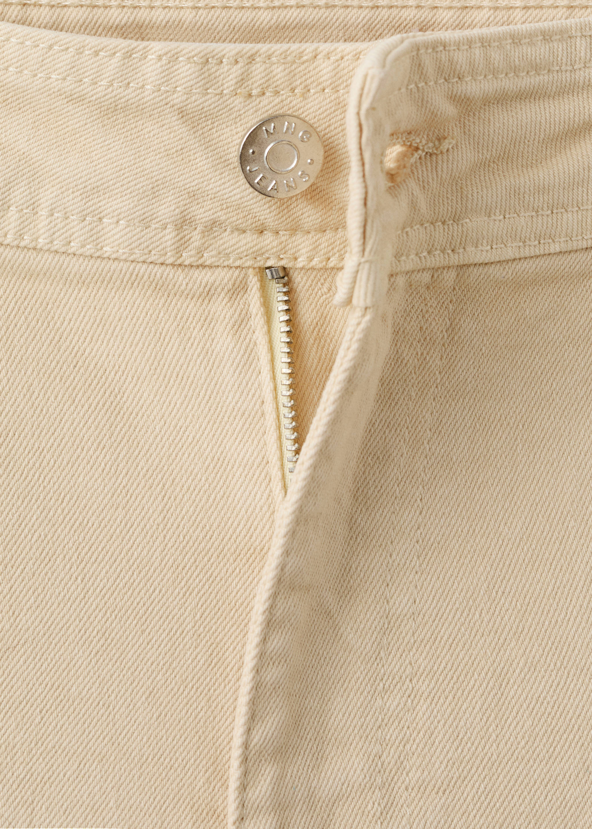 Close-up of the waistband and zip fly fastening on cream denim trousers.