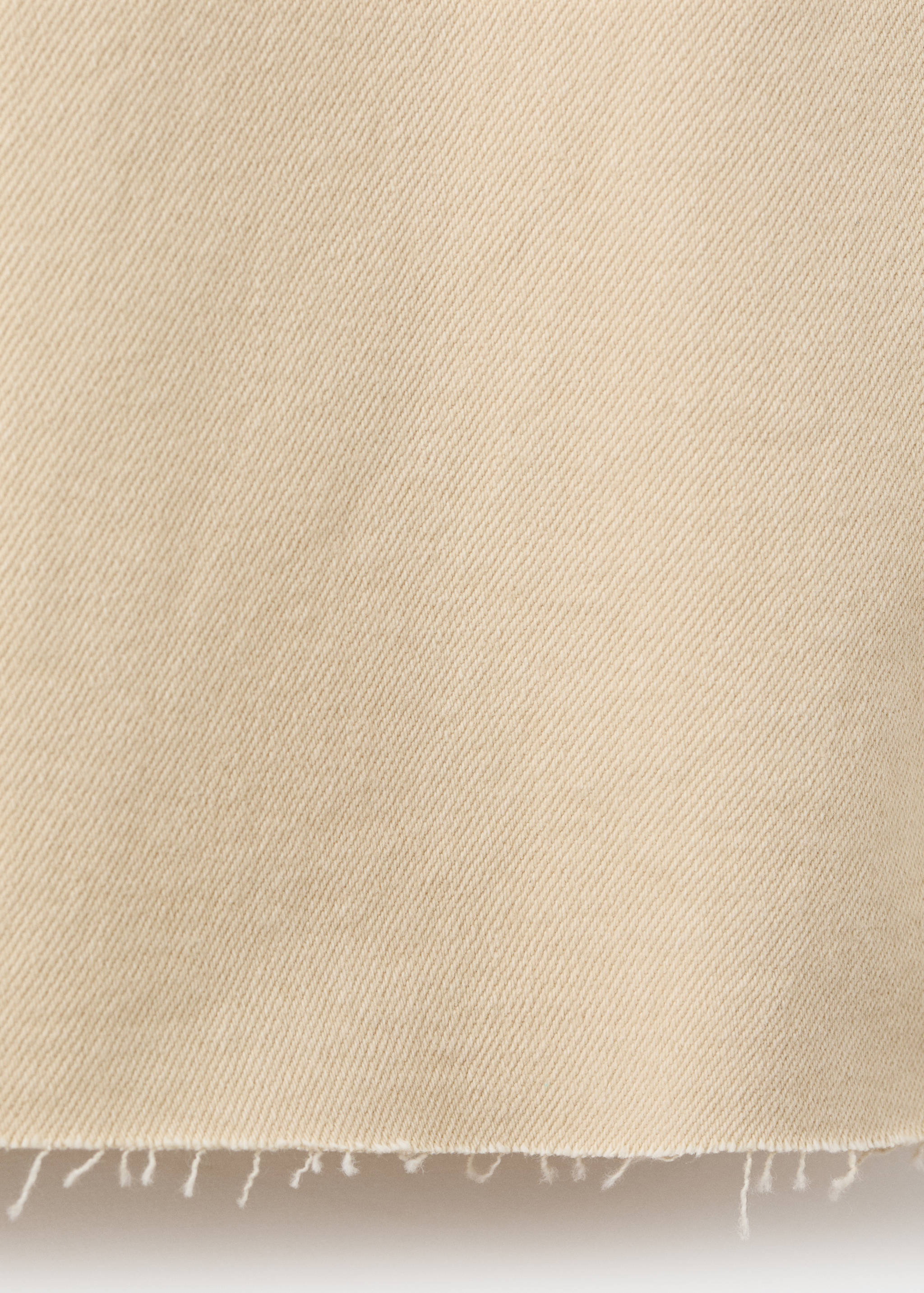 Close-up of beige denim fabric texture with a raw frayed hem.