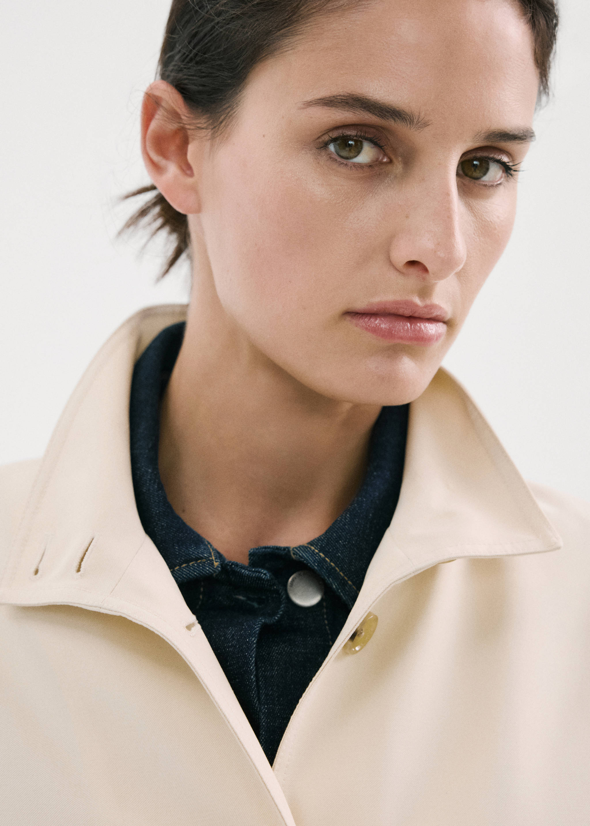 Primer plano de chaqueta beige claro con cuello estructurado sobre camisa vaquera.
