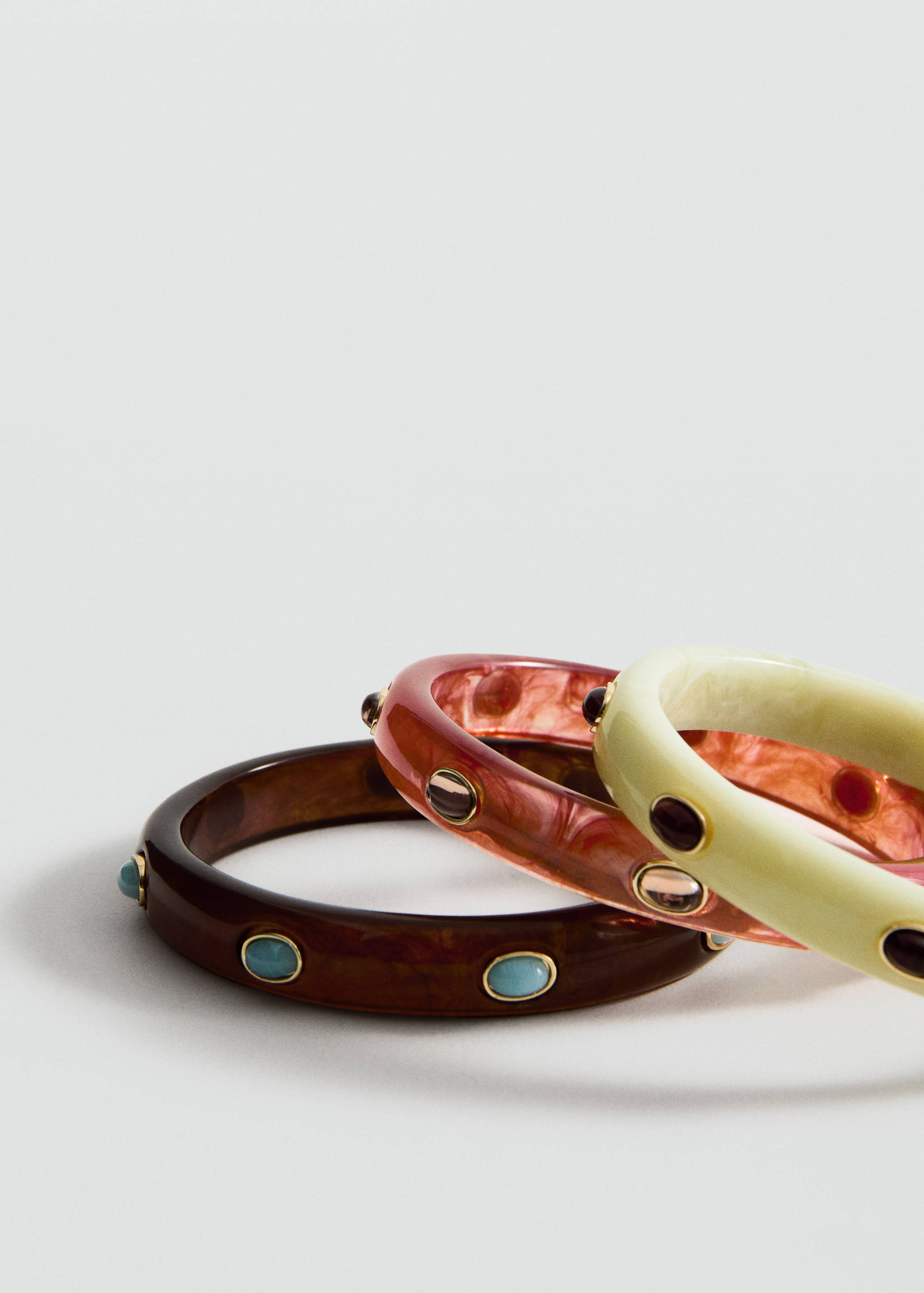 Set of three resin bangles in dark brown, pink, and cream, inlaid with stone details.