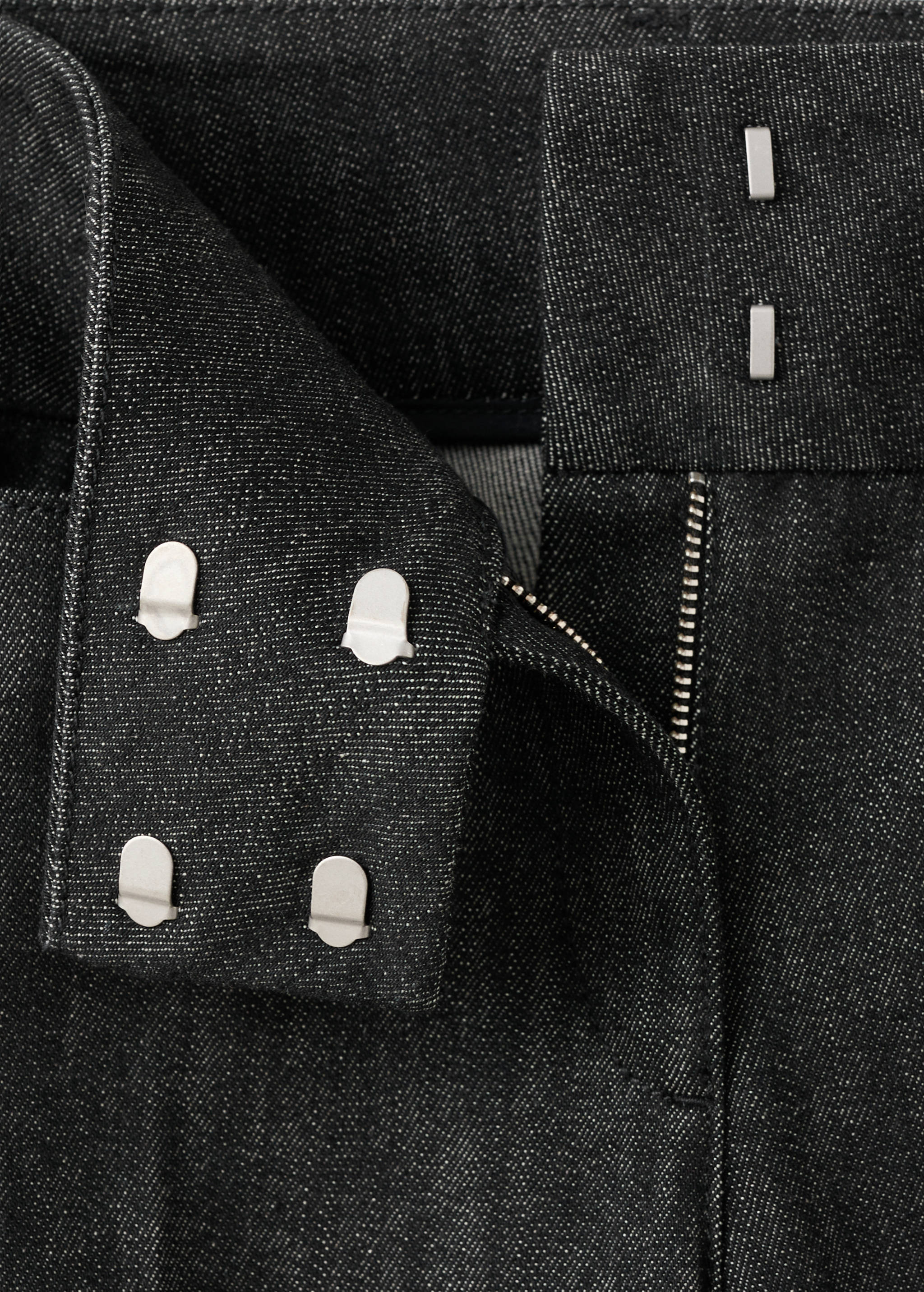 Close-up of dark grey denim trousers waistband and hook-and-bar fastening.