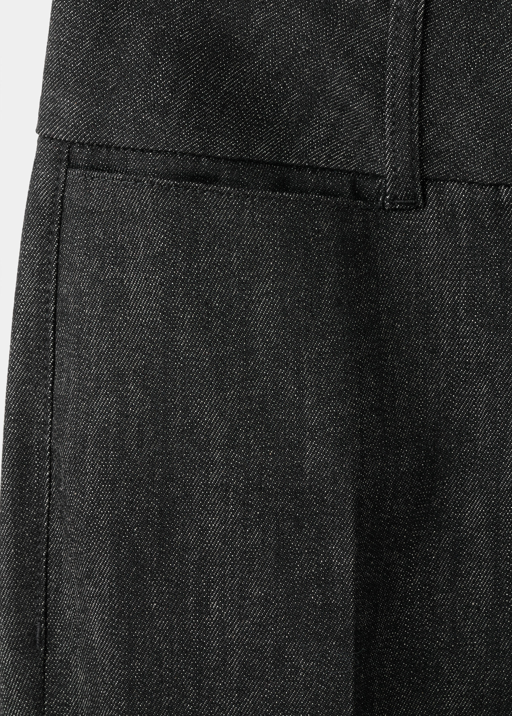 Close-up of dark grey denim fabric and waistband on women's trousers.