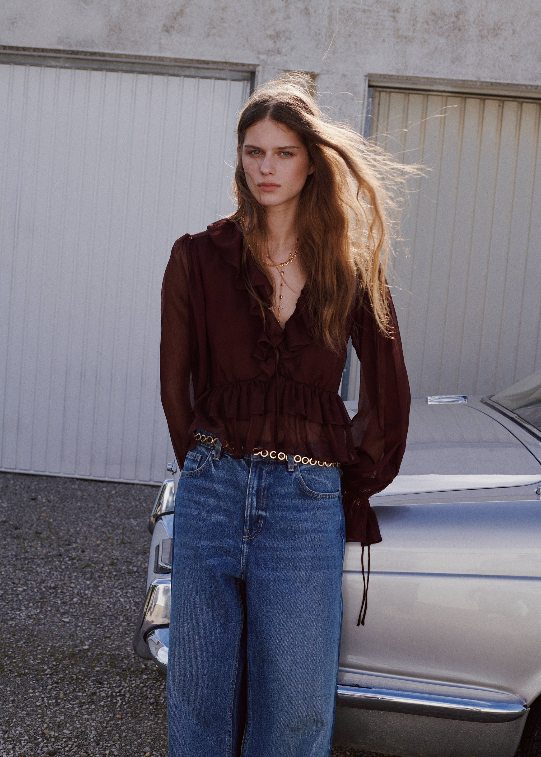Burgundy sheer ruffled blouse worn with blue denim trousers.