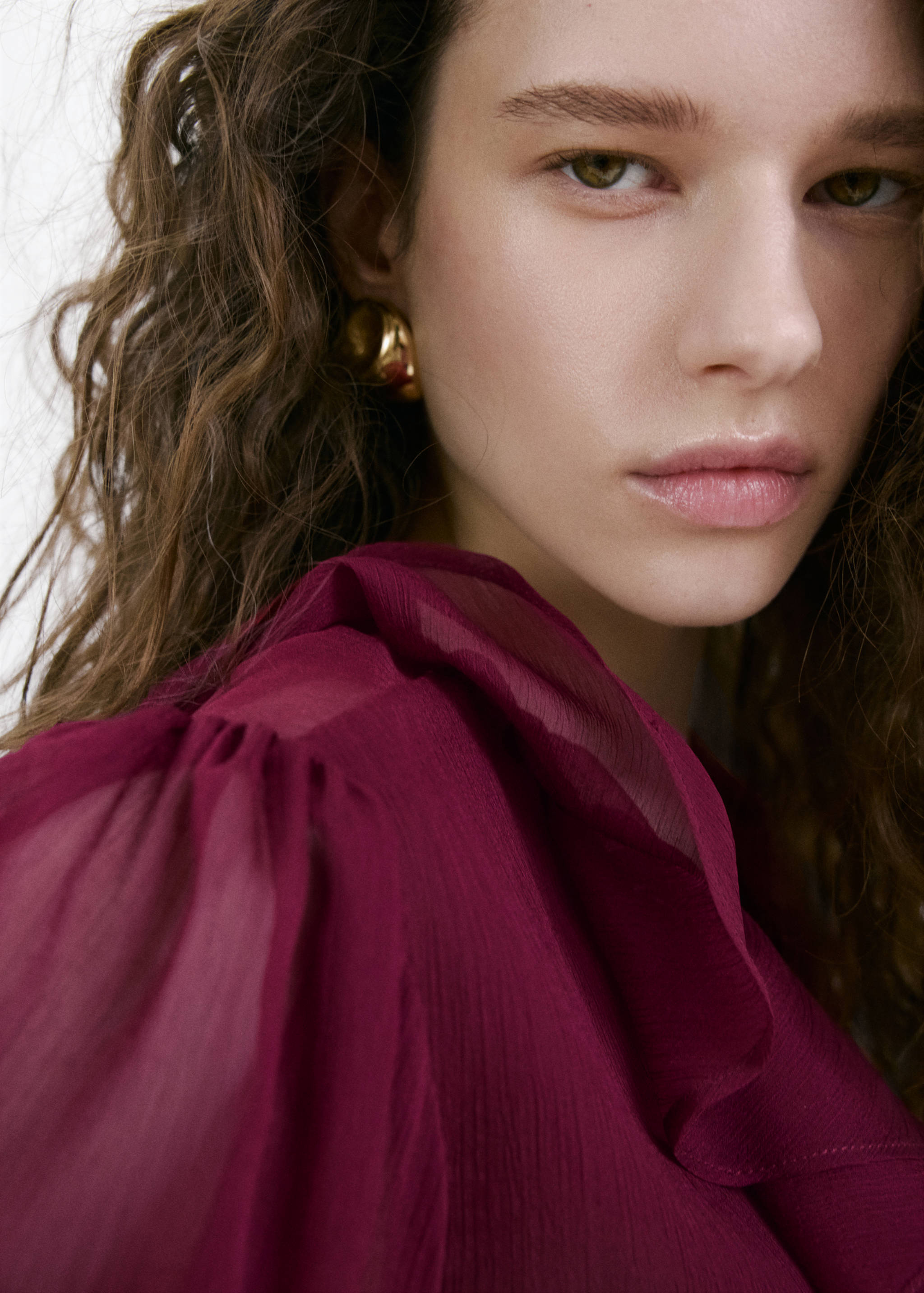 Burgundy blouse with sheer sleeves and ruffle details in close-up.