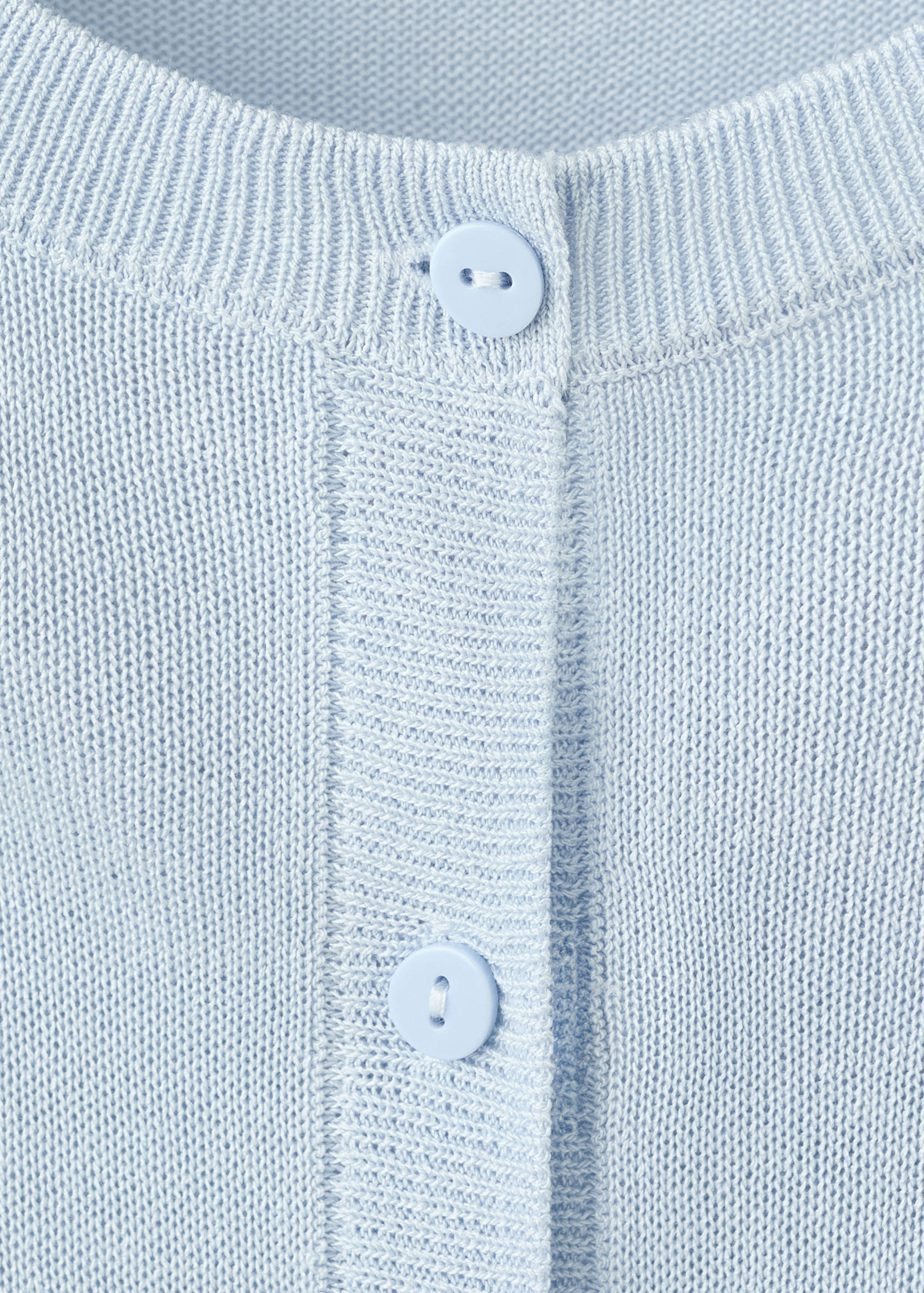 Close-up of light blue cardigan fabric detail with buttons.