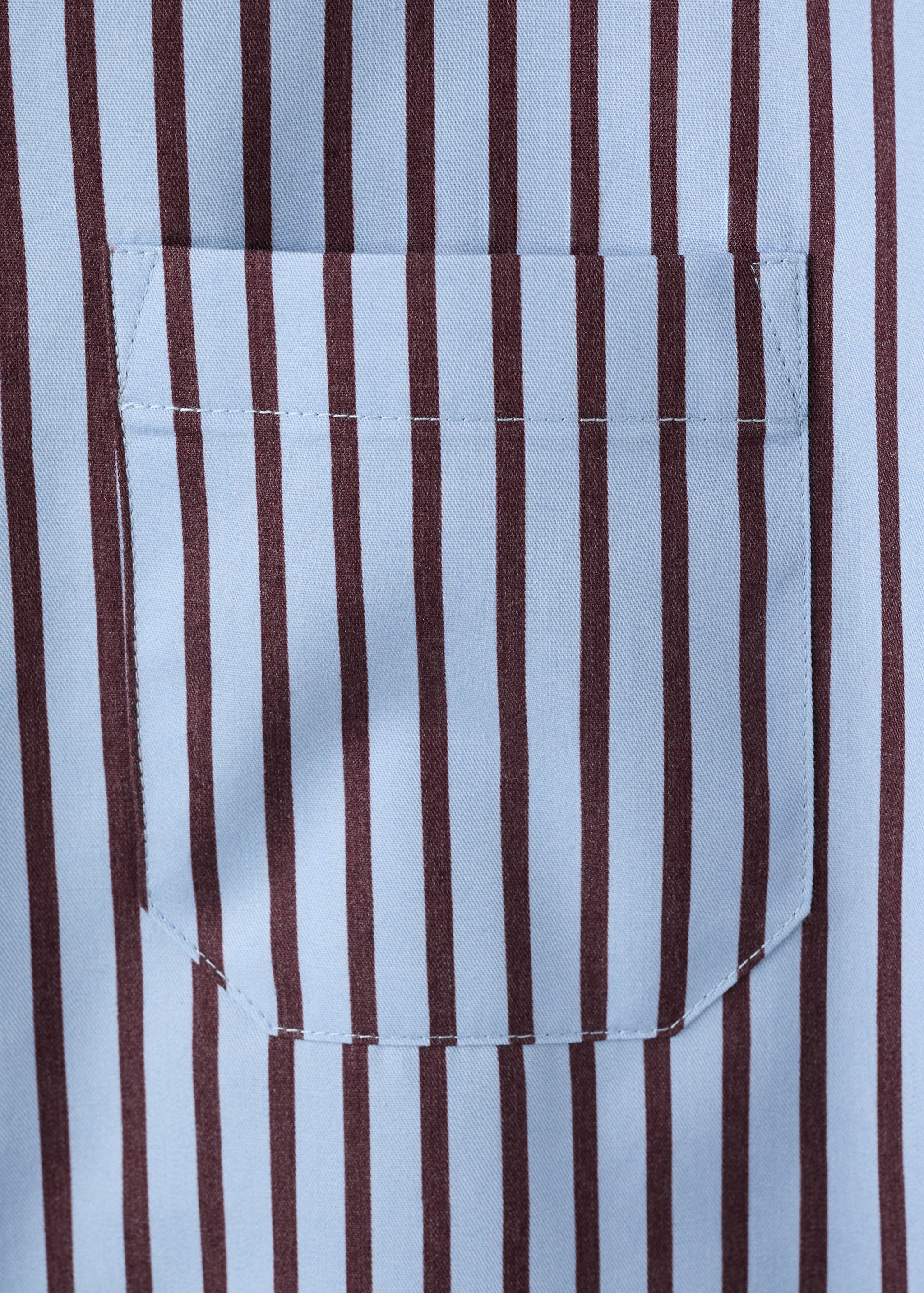 Close-up of a light blue shirt with dark brown vertical stripes and a patch pocket.