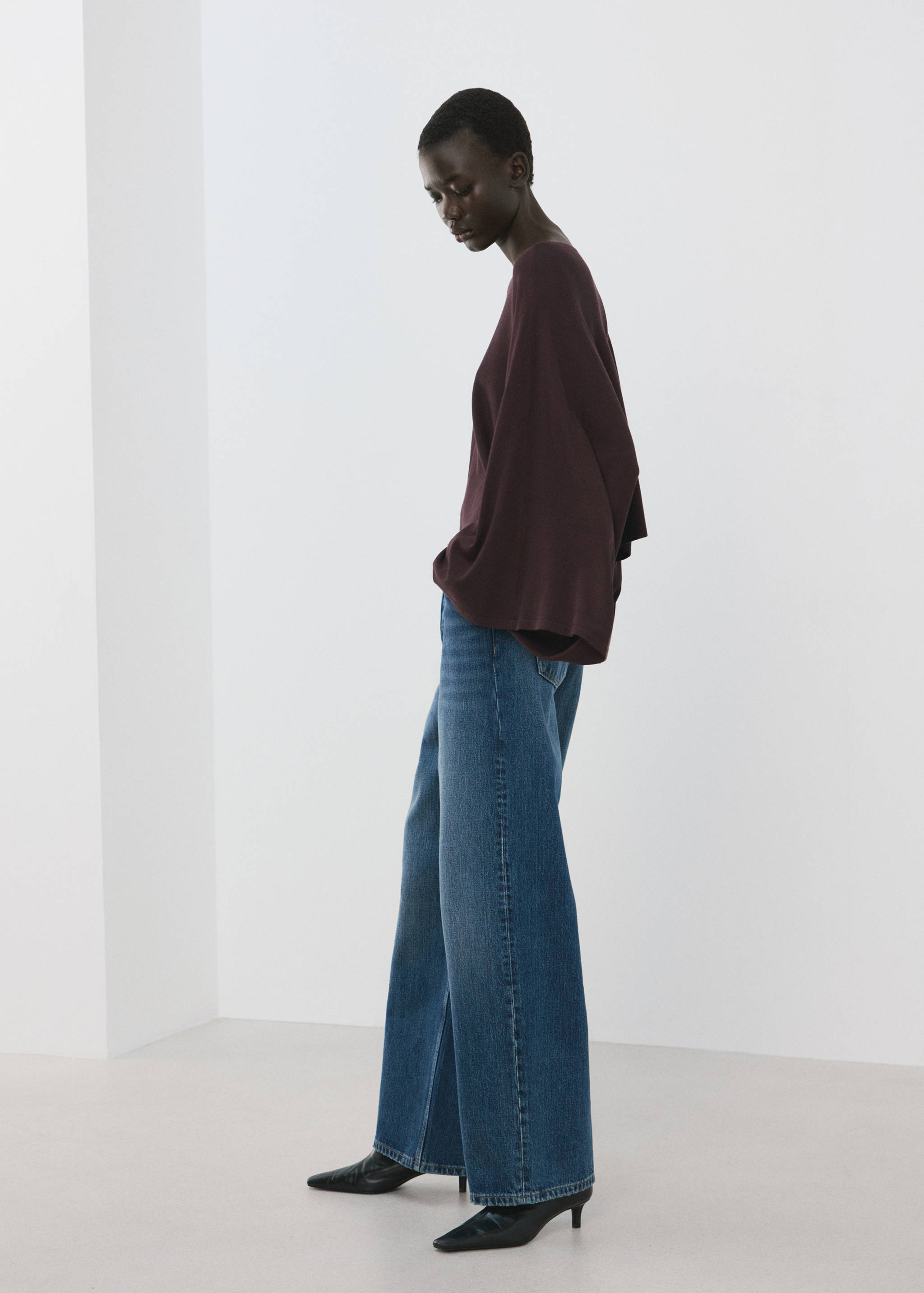 Burgundy cape with wide sleeves, worn with blue wide-leg trousers.