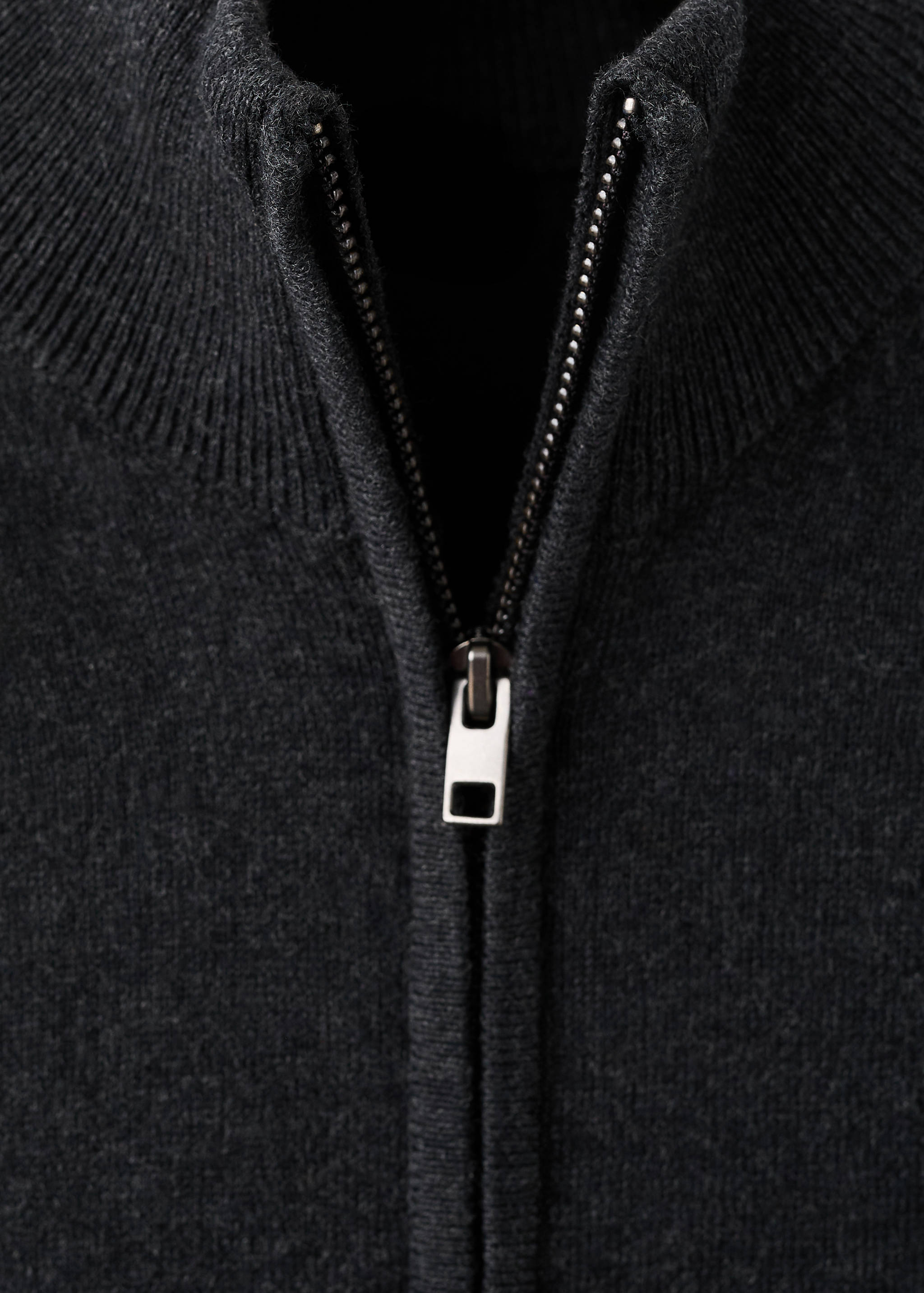 Close-up of a dark grey knit cardigan with a high ribbed collar and zip.