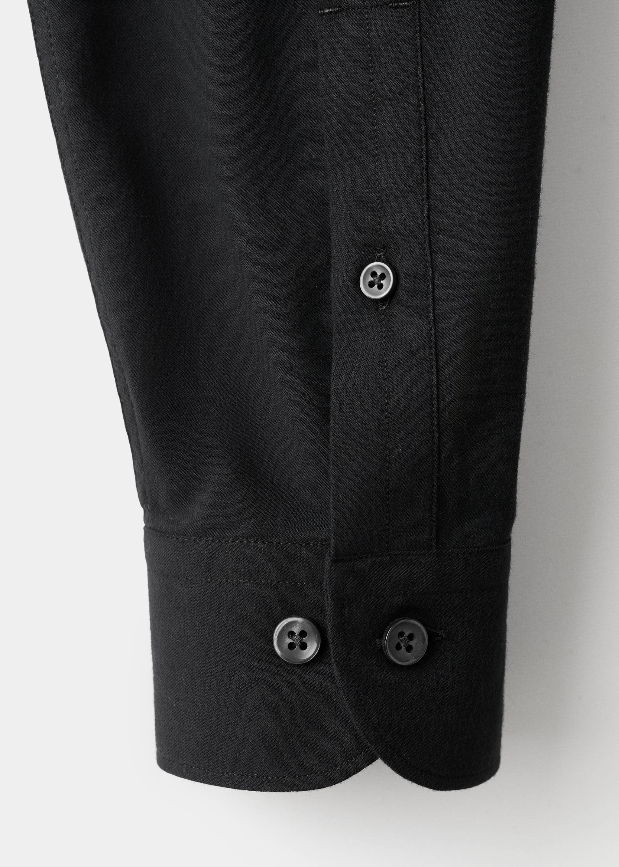 Close-up of a black shirt sleeve showing the buttoned cuff and placket.