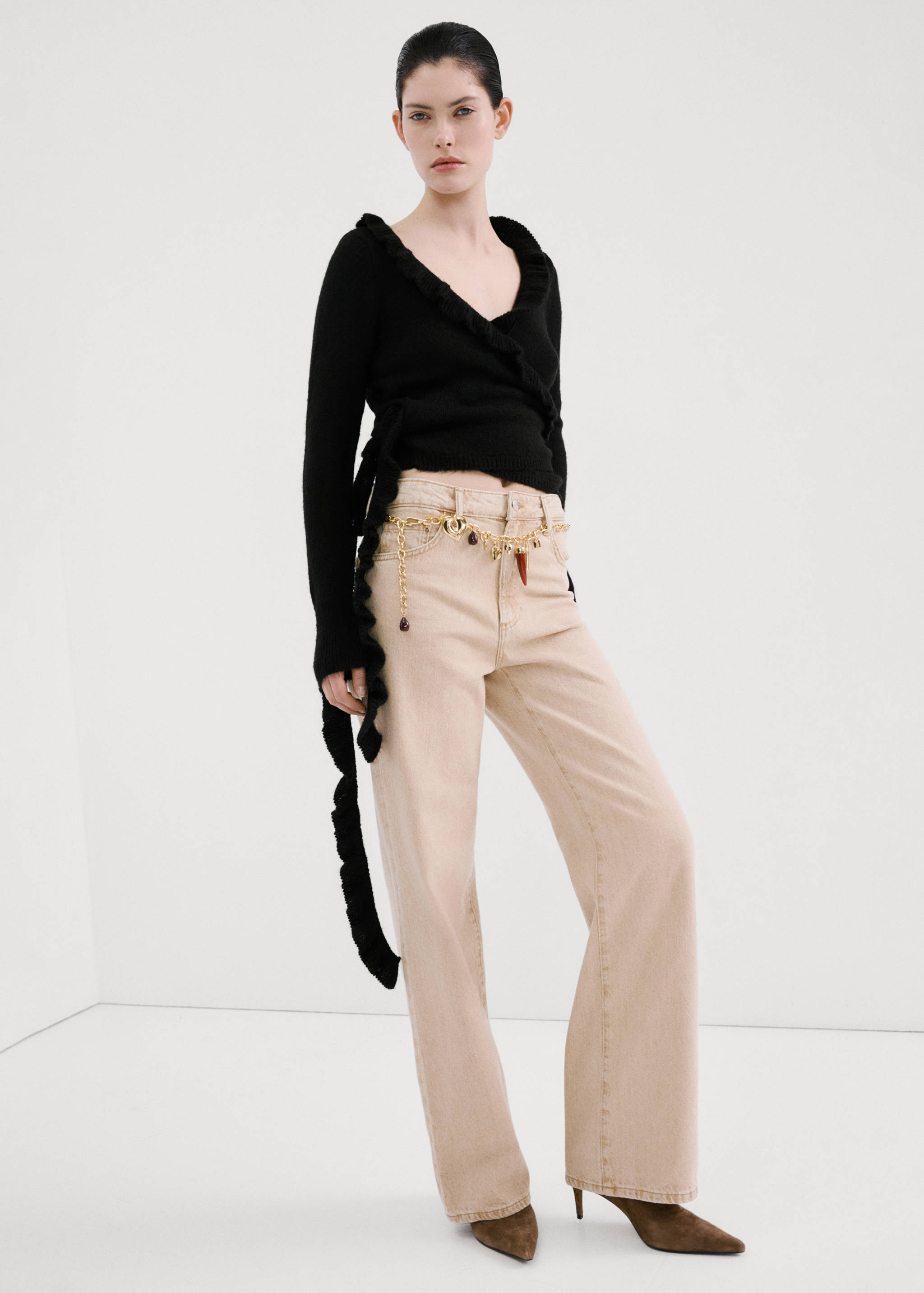Black cardigan with wrap-style V-neck and ruffles, worn with beige trousers.