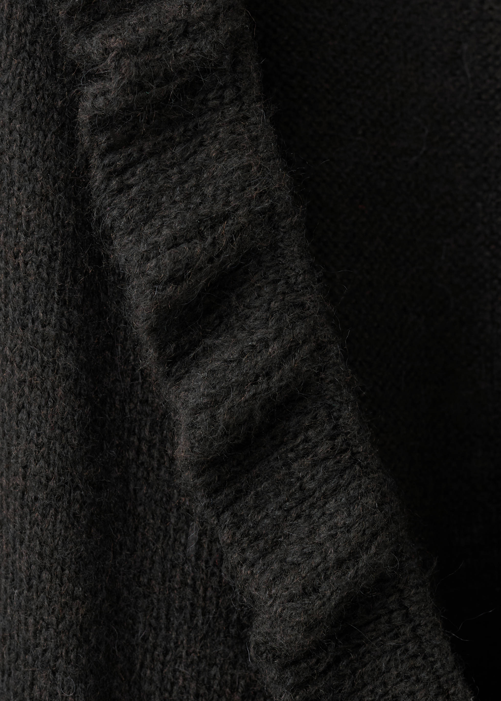 Close-up of a black knitted cardigan with a ruffled trim.