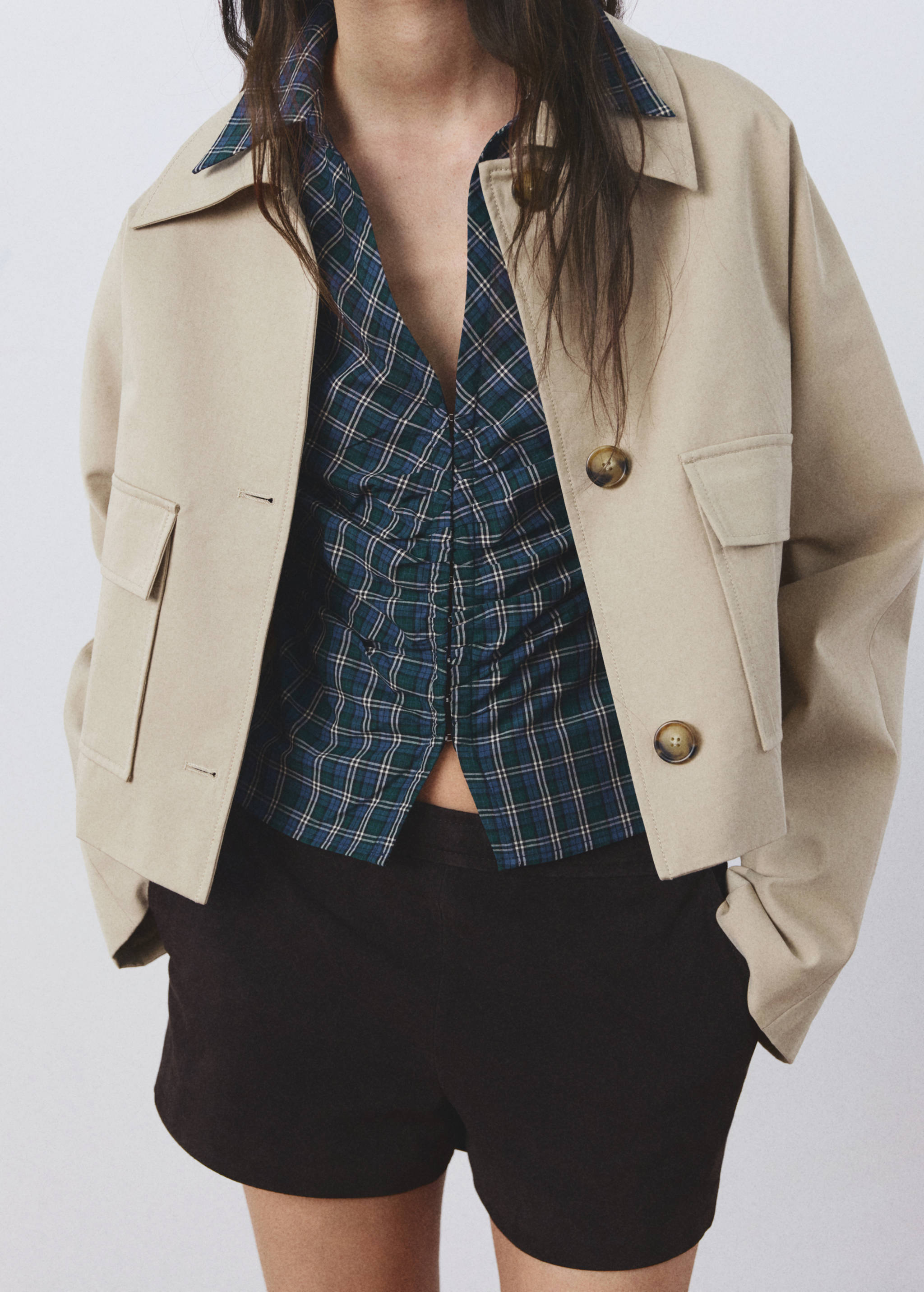 Green and blue plaid blouse with central ruching, layered under a beige jacket.
