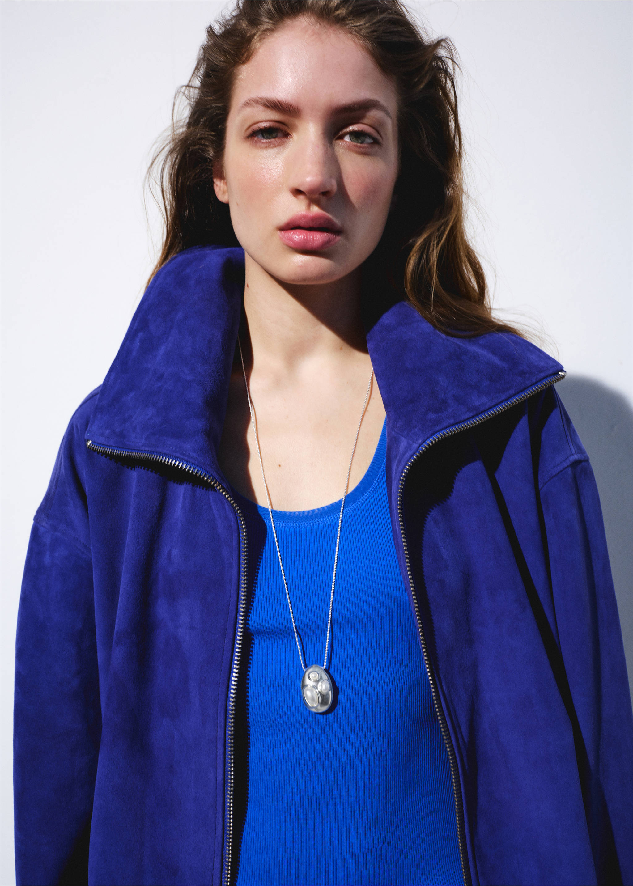 Blue suede zip-up jacket with a high collar, worn with a blue top and necklace., Silver. Ref: 27087796-00.